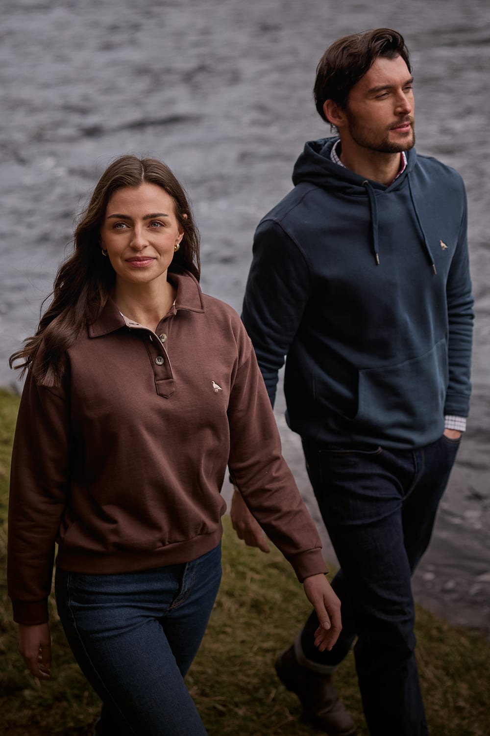A man and a woman walking outdoors wearing blue and brown sweaters