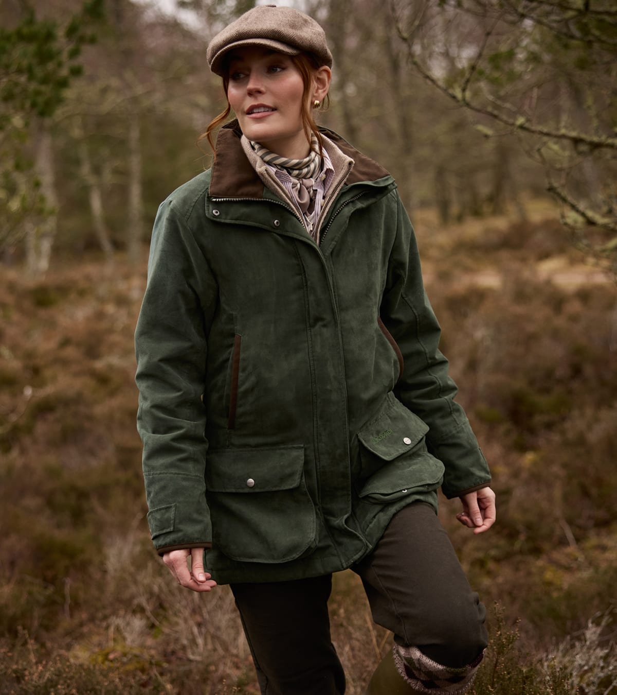 Woman walking through a woodland wearing a green shooting coat and tweed cap