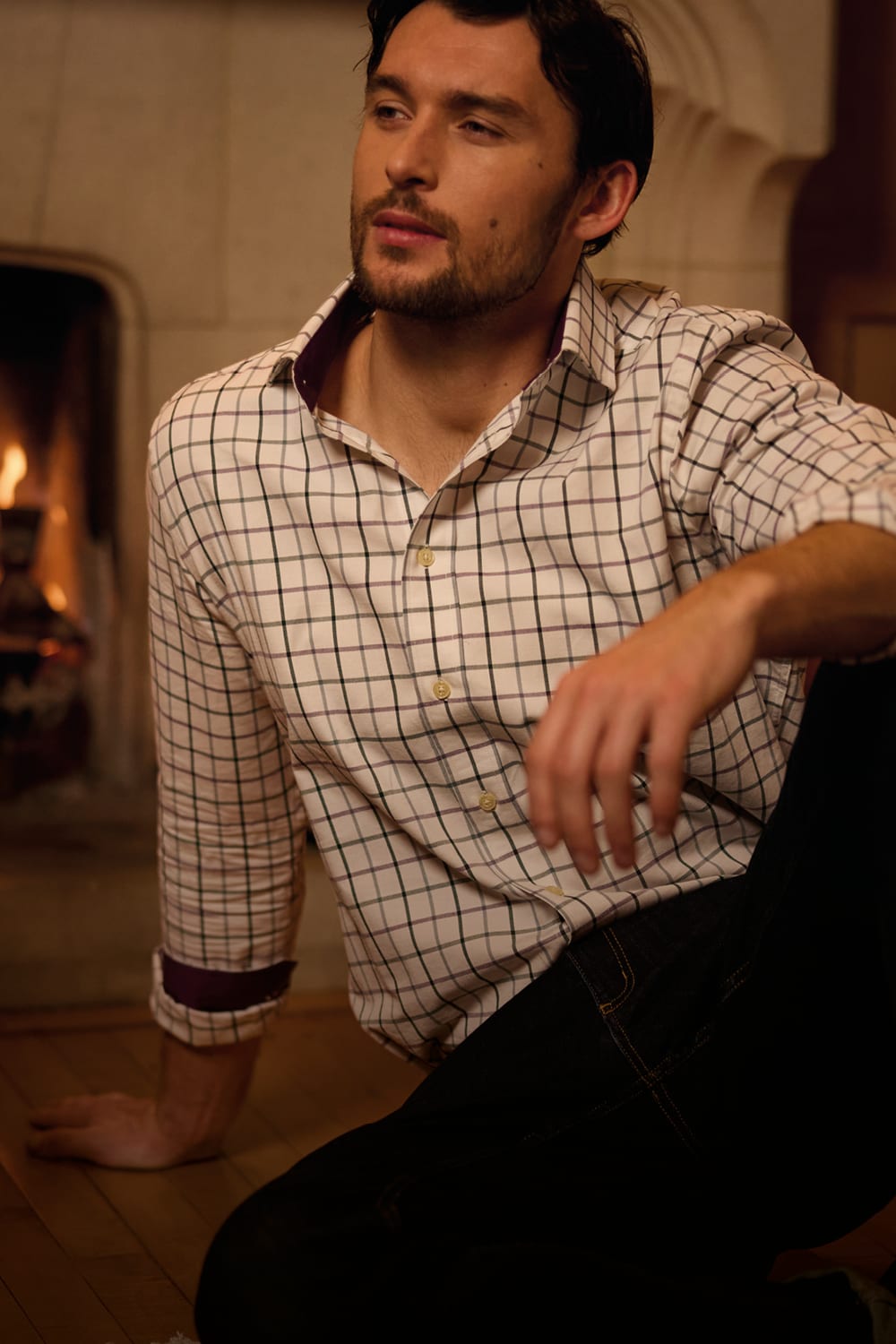 Man sitting by a fire wearing a cream checked shirt and dark jeans