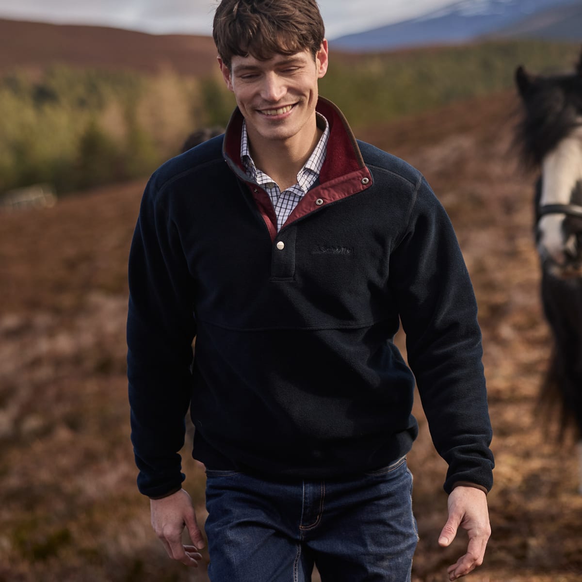Man walking across moorland wearing a navy fleece pullover with a burgundy collar