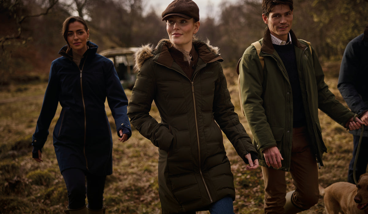 Three people wearing winter parkas walking through woodland with a dog.