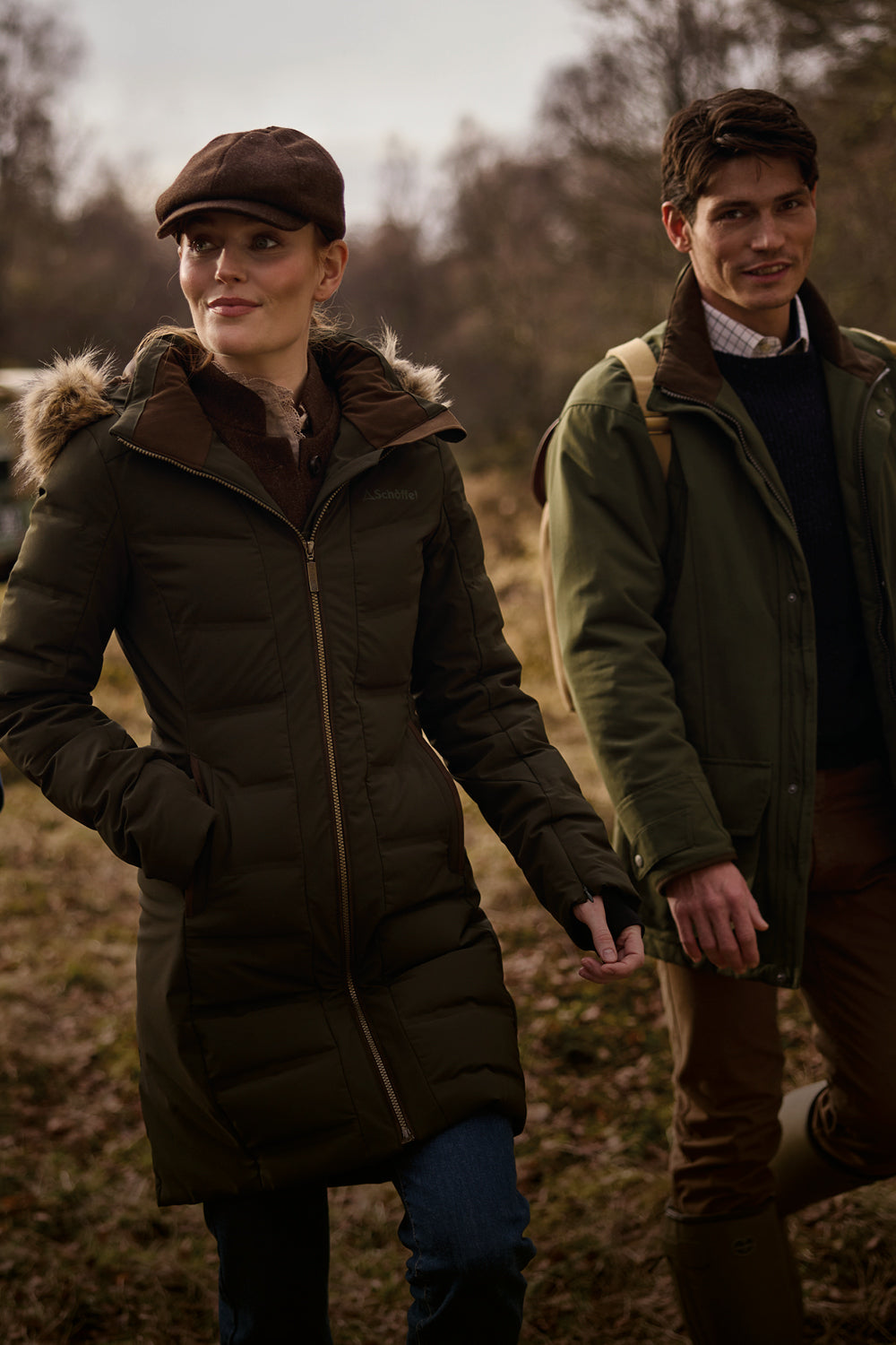 Woman in a brown fur-trimmed puffer coat and flat cap walking with a man in an olive jacket.