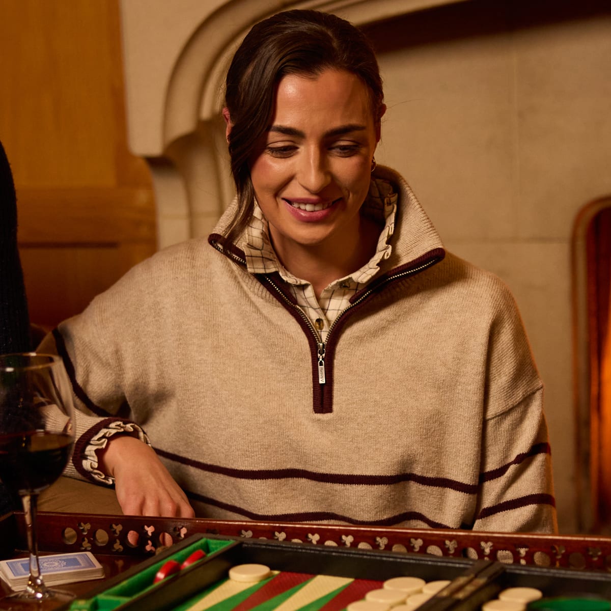 Woman wearing a beige striped half-zip sweater with a checked collar while playing backgammon.