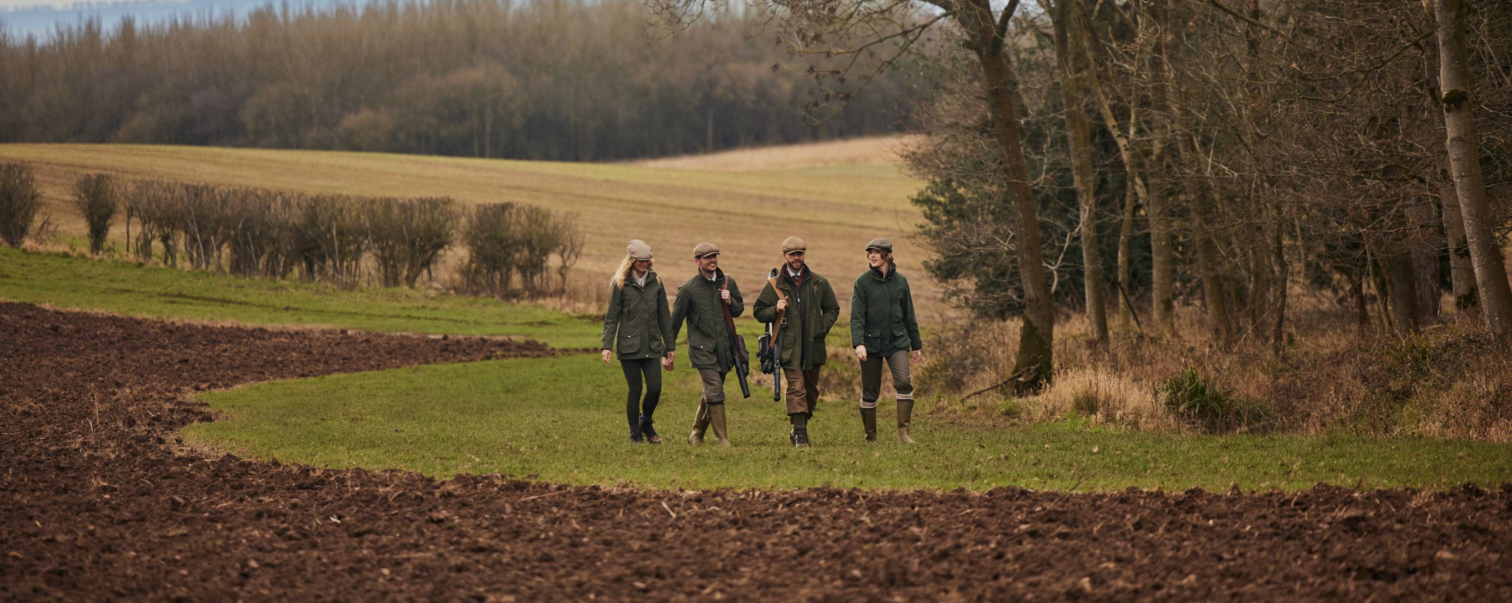 A group of people walking in a field wearing countrywear.