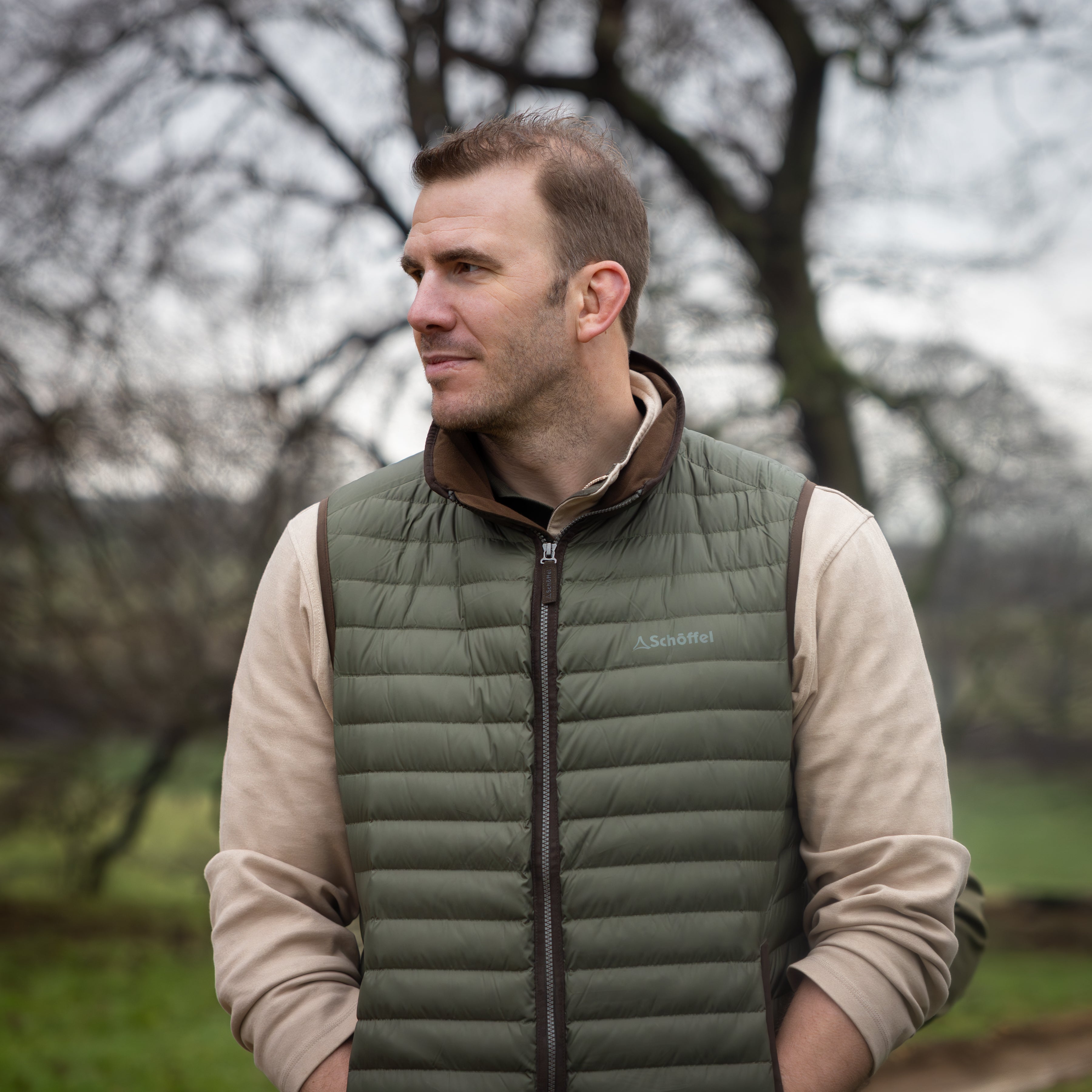 Tom Croft wearing a green gilet over a beige sweatshirt looking slightly to the right