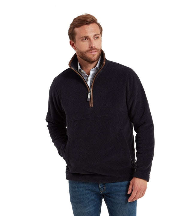 A man wearing a navy fleece quarter-zip pullover with tan leather-trim zip and a stand collar, paired with a checked shirt and blue jeans.