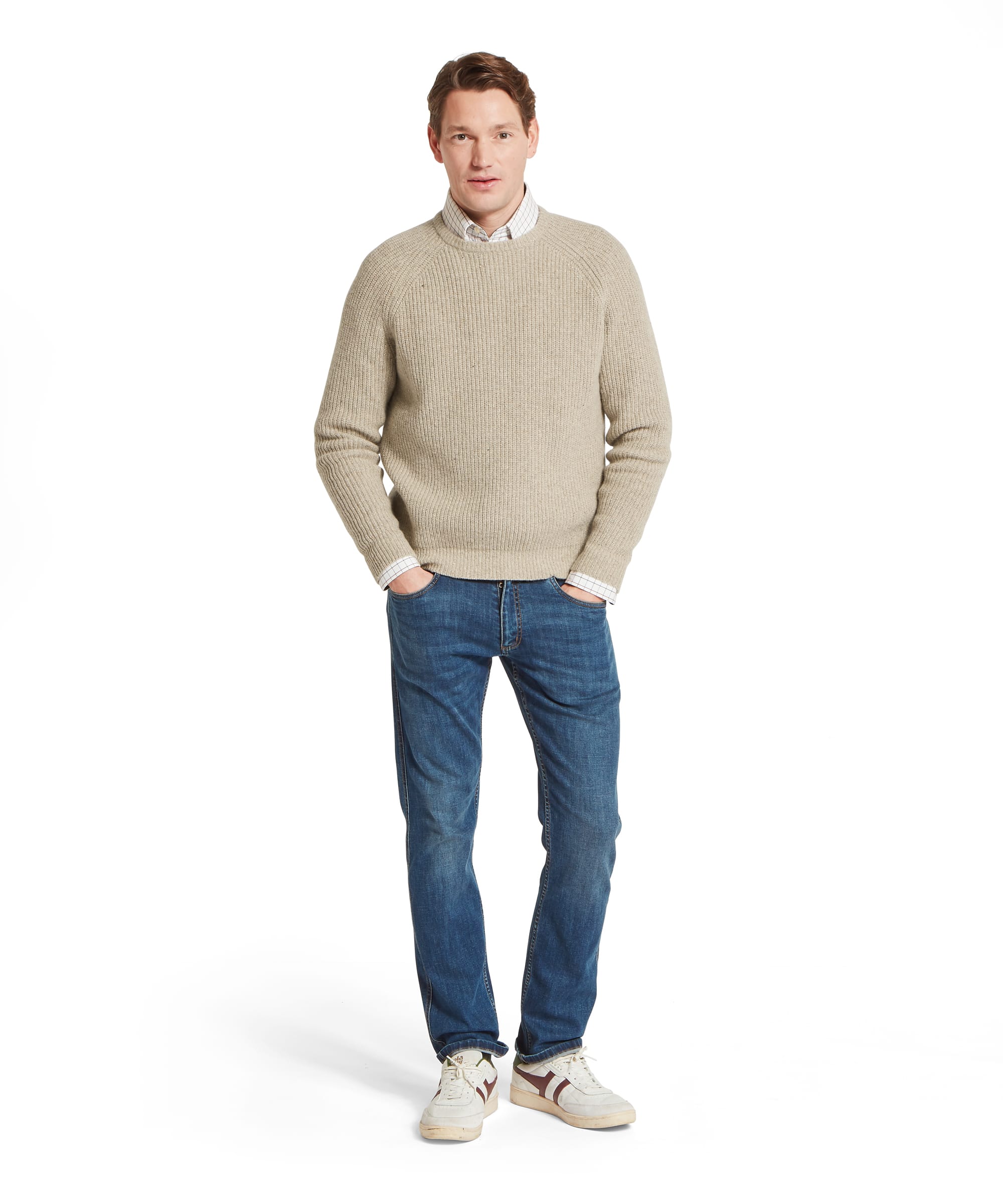 Schöffel Men's Balmaha Crew Neck Jumper in Beige - full-length front view of a relaxed oatmeal ribbed lambswool crew neck jumper layered over a check shirt, worn with blue jeans and white Gola trainers.
