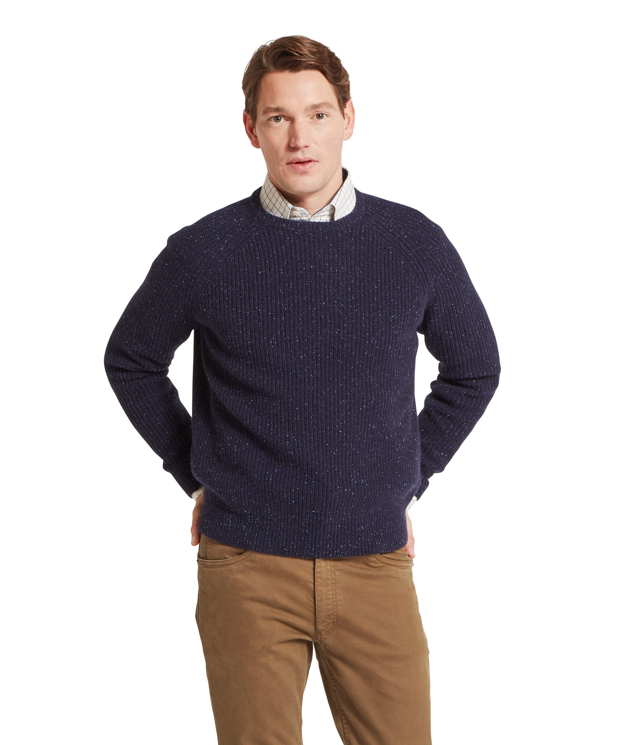 Schöffel Men's Balmaha Crew Neck Jumper in Blue - three-quarter front view of a chunky ribbed navy donegal lambswool crew neck jumper with raglan sleeves, layered over a check shirt, worn with khaki trousers and Reebok trainers.