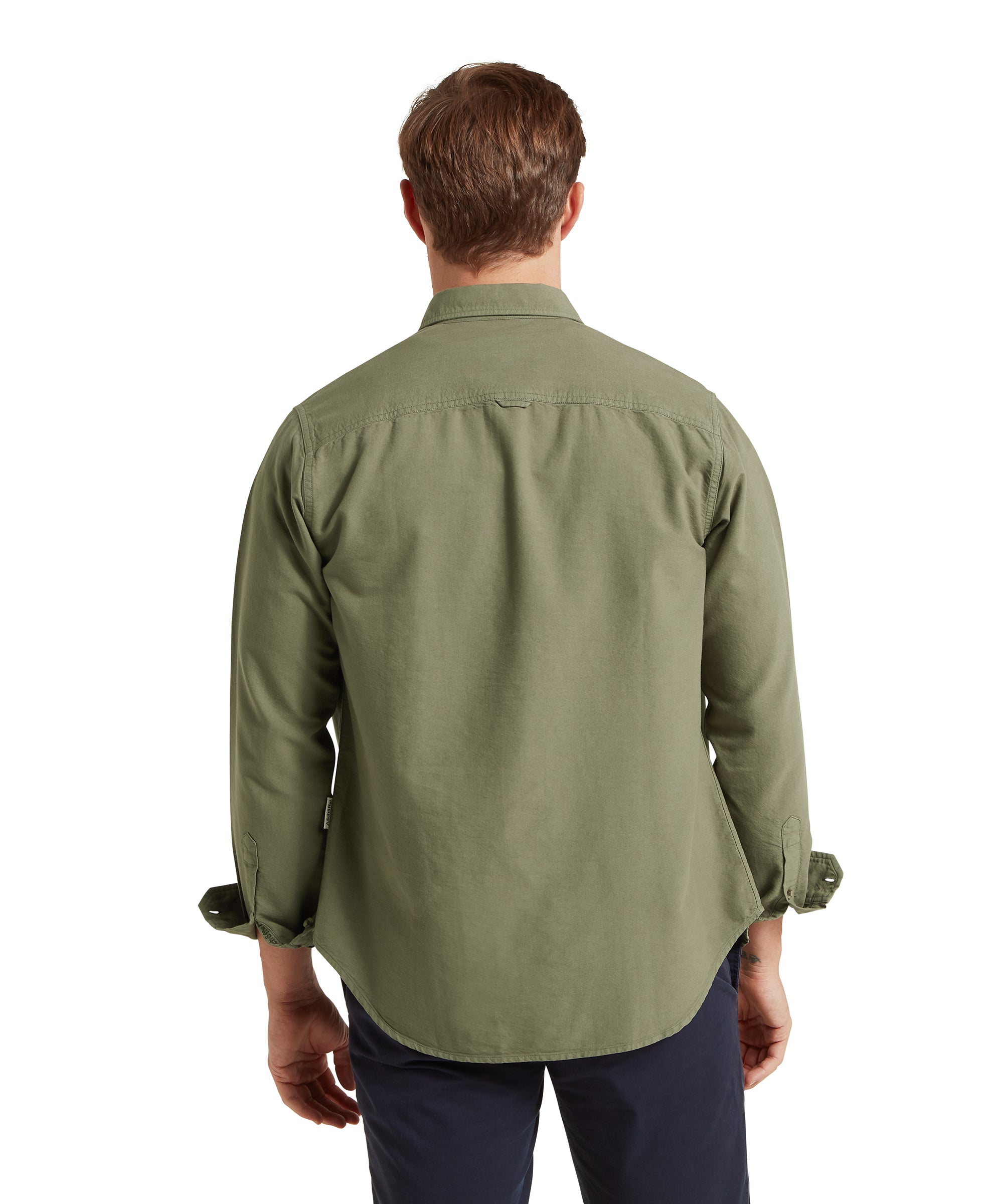 Back view of a man wearing a long-sleeved olive green button-up shirt with a straight yoke across the shoulders, paired with dark trousers. The shirt appears to be made from a casual cotton or cotton-blend fabric, and the sleeves are rolled up slightly and buttoned at the cuffs. He has short brown hair, and the plain white background highlights the shirt’s fit and structure.