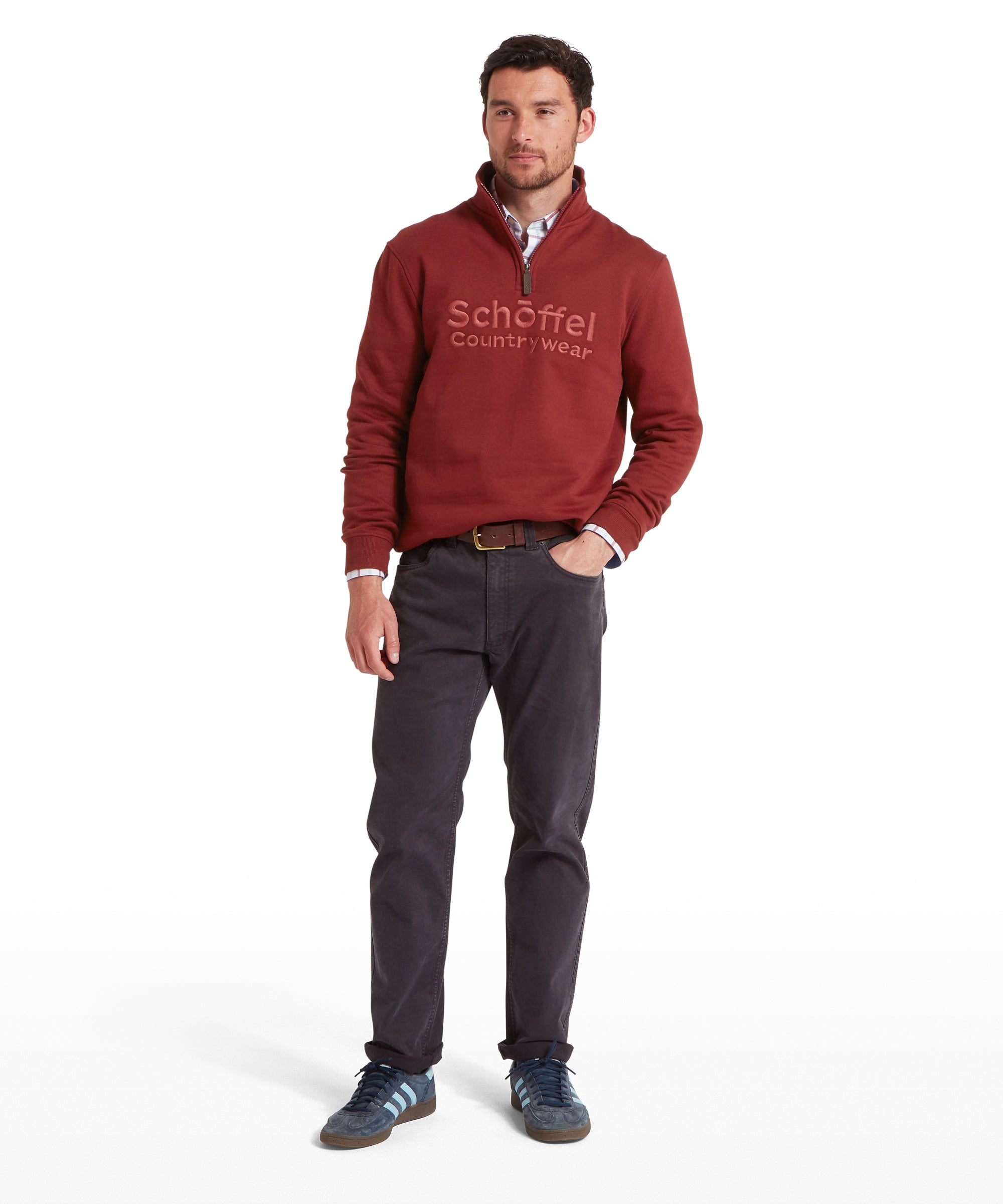 Man wearing a red sweater with 'Schöffel' logo and dark pants on a white background