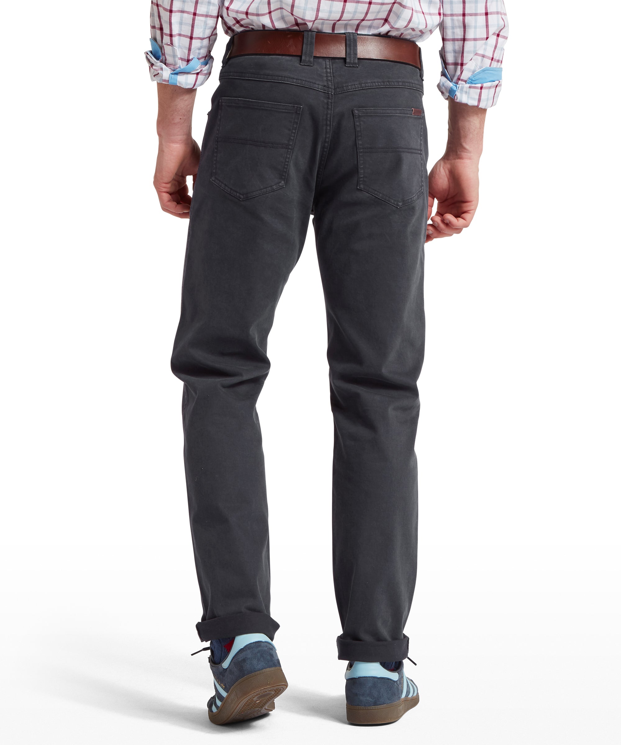 Rear view of a man wearing a plaid shirt with rolled-up sleeves, tucked into dark grey trousers, styled with a brown belt and multicoloured trainers. Trousers feature stitched back pockets and are cuffed at the ankles. Pose shown on a transparent background.