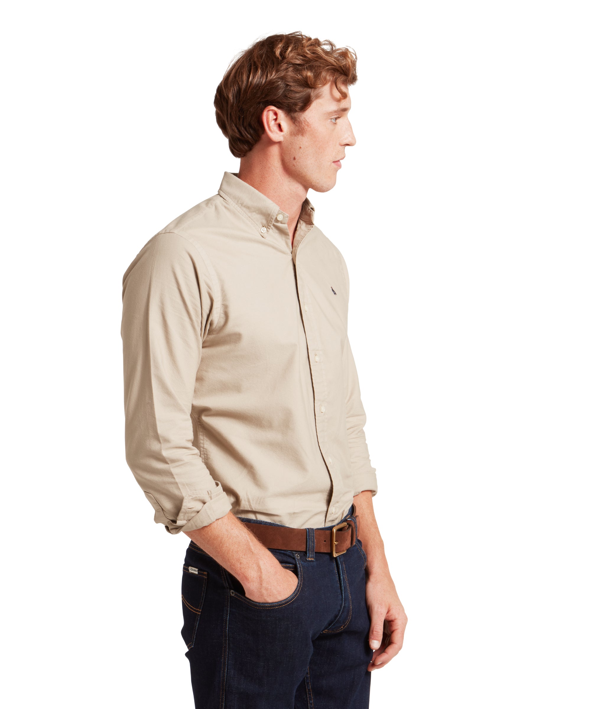 Man wearing a beige shirt and dark jeans on a white background