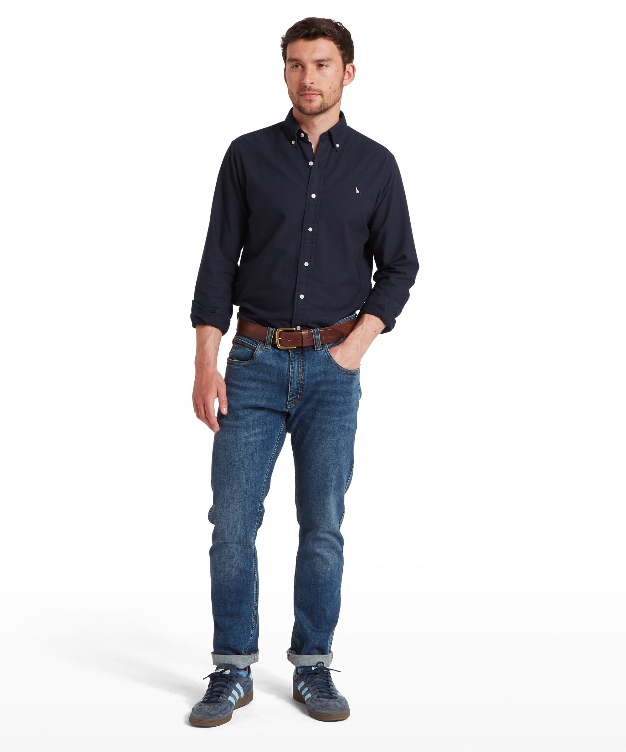 Man wearing a navy button-up shirt and blue jeans on a white background