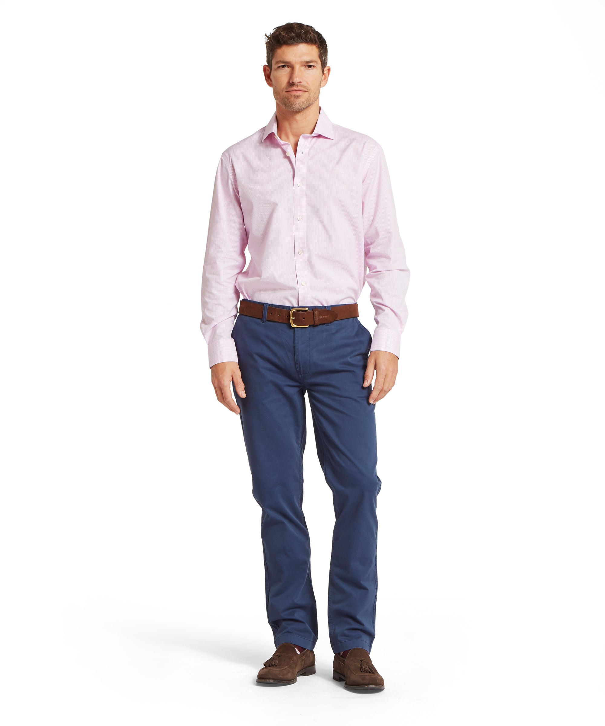 Man wearing a pale pink shirt tucked into dark navy jeans, styled with a brown belt and brown suede shoes. Outfit shown in a relaxed standing pose on a plain white background.