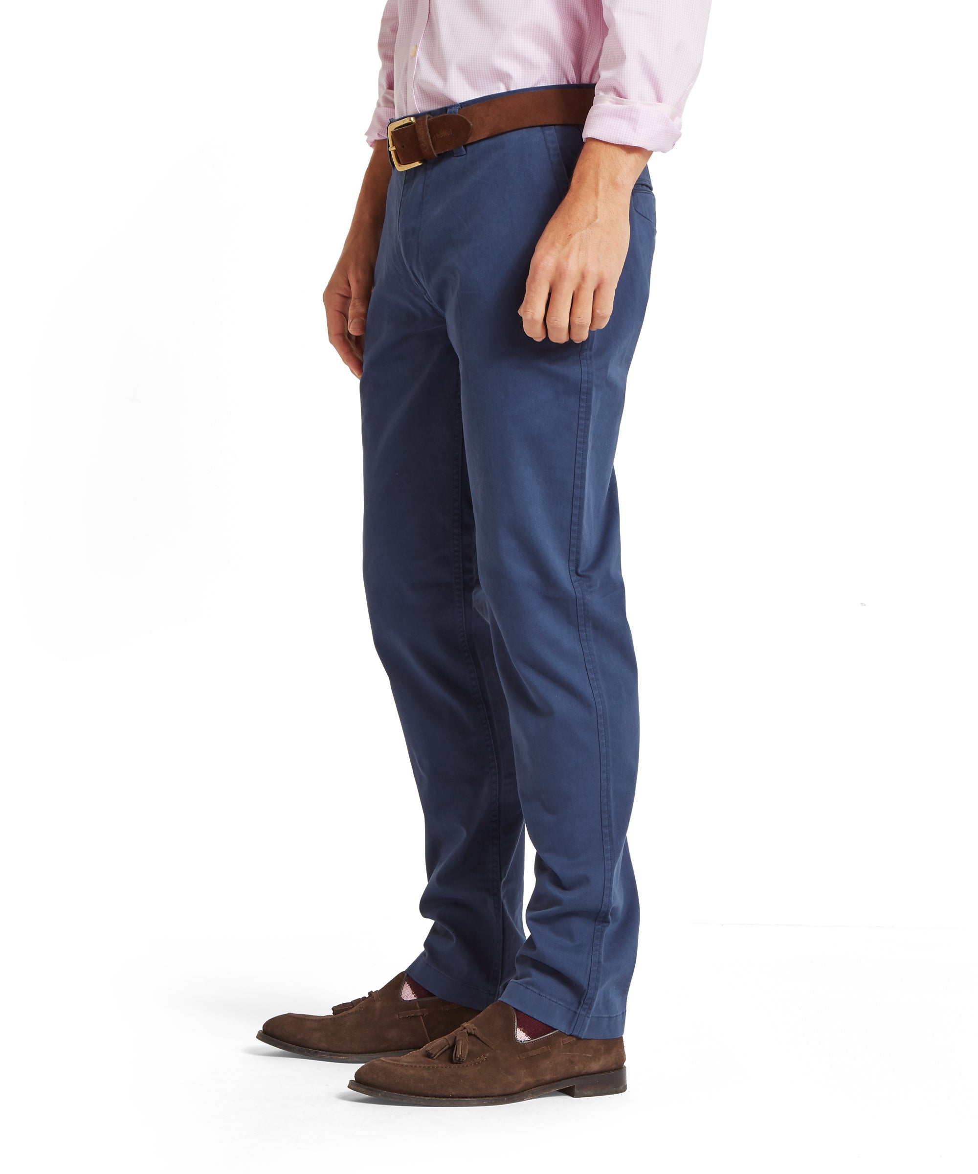 Side view of a man wearing a pale pink shirt tucked into blue chinos, styled with a brown belt with gold buckle, maroon patterned socks and brown suede tassel loafers. Image focuses on the lower half of the body, shown on a plain white background.