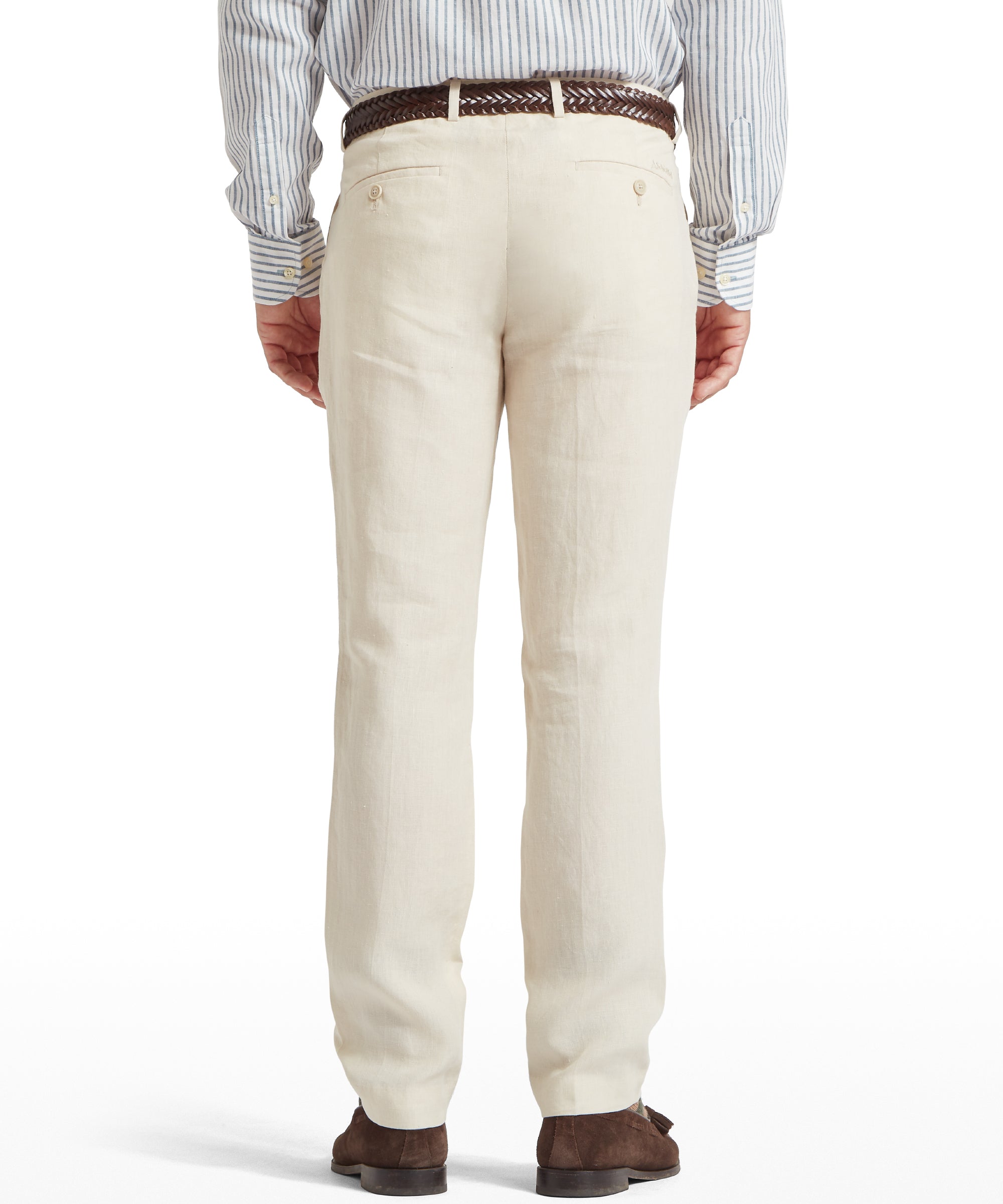 Back view of a man wearing cream linen trousers with two buttoned back pockets. Paired with a light blue and white striped long-sleeved shirt, a brown woven belt, and brown shoes. Standing upright against a plain white background.