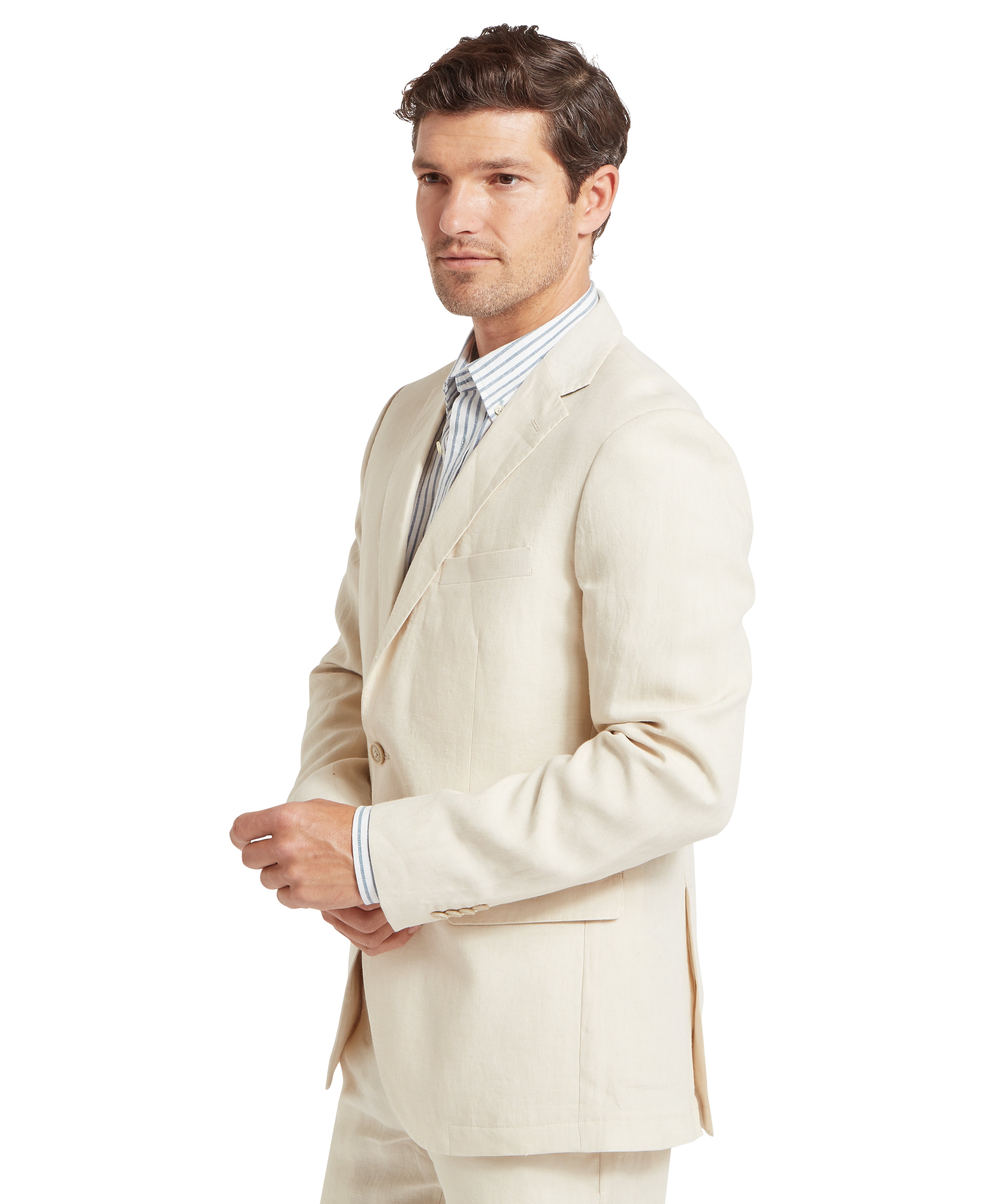 Man wearing a cream suit with a matching blazer and trousers. The blazer features a notched lapel, a chest pocket, and two lower front pockets. Underneath is a light dress shirt with vertical stripes. He is standing in a semi-profile pose with hands loosely clasped in front. The outfit is formal and tailored, suitable for business or fashion-forward occasions.