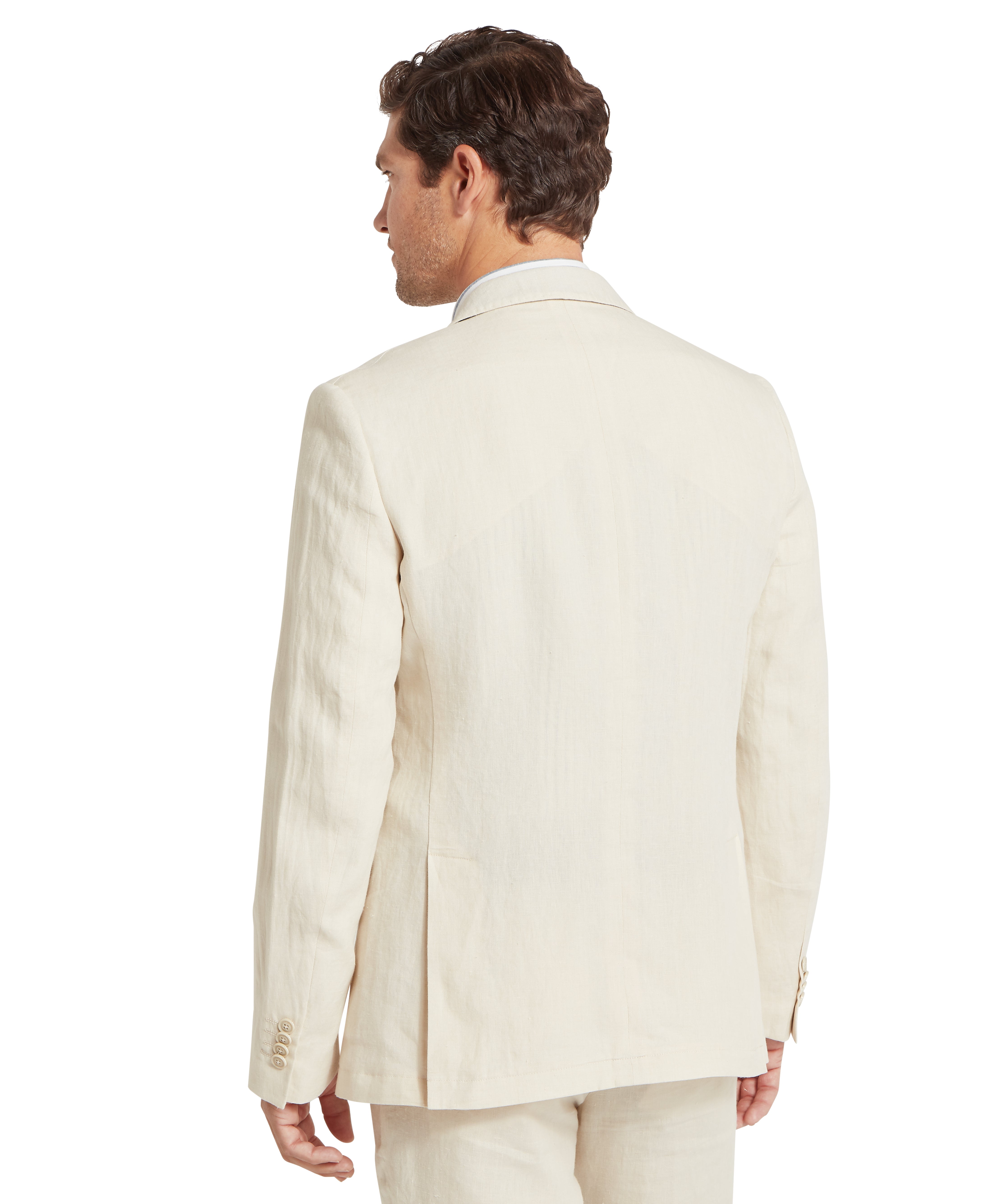 Man wearing a cream linen suit, viewed from the back. The tailored jacket features a centre seam, two side vents, and four buttons on each cuff. The collar is neatly structured, and he is also wearing matching trousers. He has short, wavy brown hair and stands with a relaxed posture. The image highlights the back design and fit of the formal suit, suitable for retail or tailoring contexts.