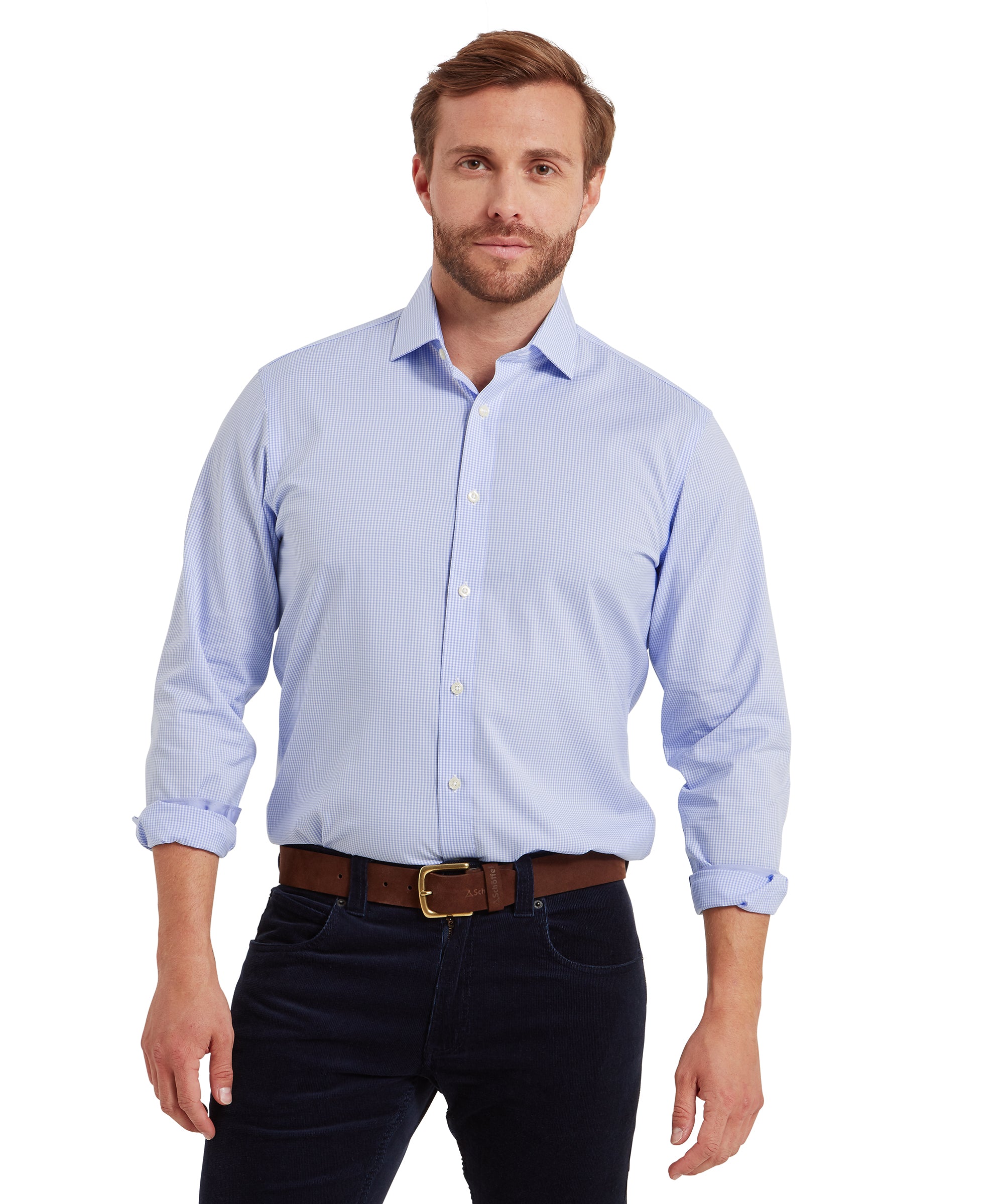 Man wearing a light blue, long-sleeved, button-down shirt with a subtle check pattern. The shirt is tucked into dark trousers and secured with a brown leather belt featuring a gold buckle. The sleeves are rolled up to the forearms. He is standing facing forward against a plain white background. The outfit is smart-casual, suitable for professional or social settings.