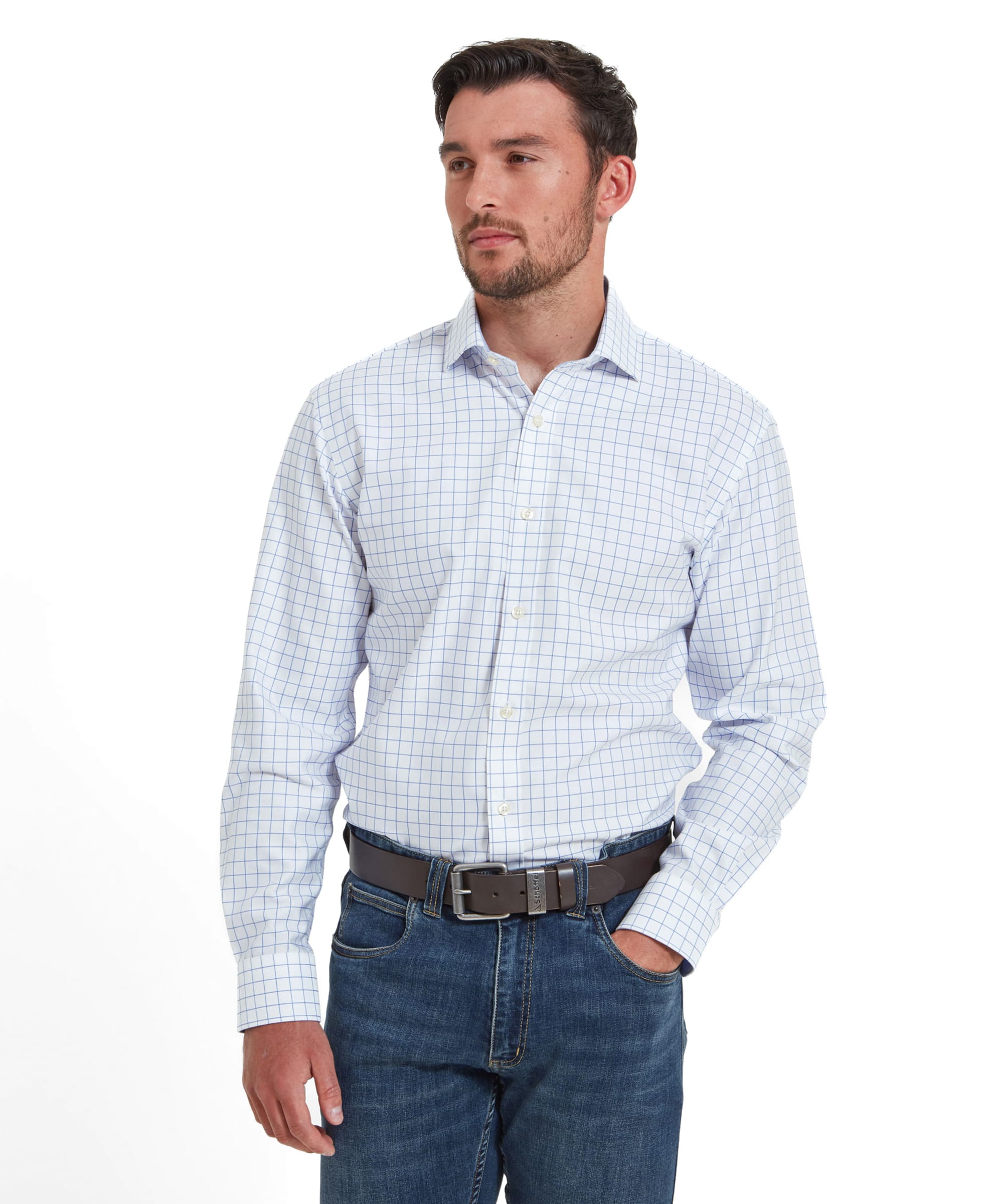 A man is wearing a Schoffel Greenwich Tailored Shirt for Men in Blue Check. He is standing with his hands in his pockets, looking slightly to the right with a neutral expression.