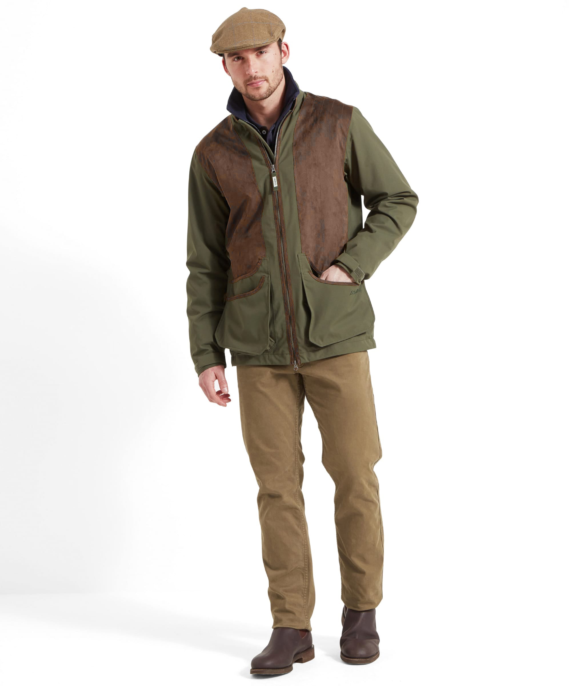 Man wearing the Schöffel Grimsthorpe Clay Shooting Jacket in Green with a tweed flat cap, full-length front view with chinos and leather boots.