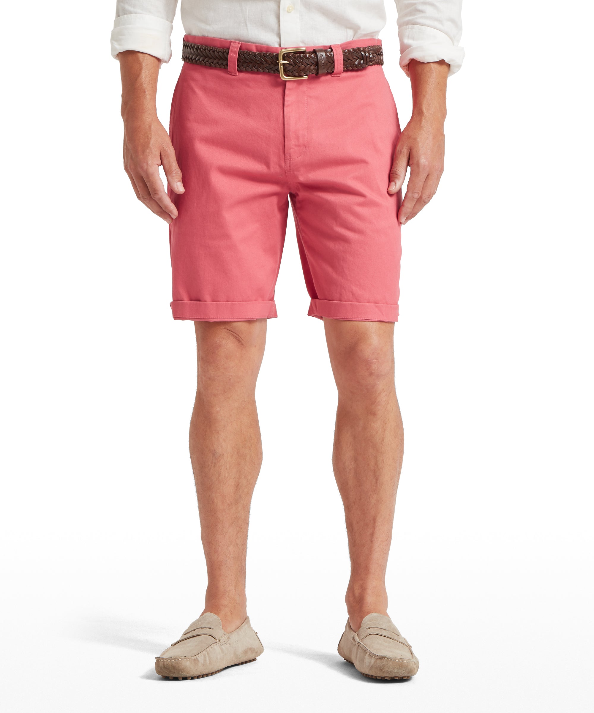 Man wearing pink knee-length shorts with a cuffed hem, paired with a white long-sleeved shirt tucked in. Styled with a brown woven belt featuring a gold buckle and beige suede loafers. Standing front-facing against a plain white background.