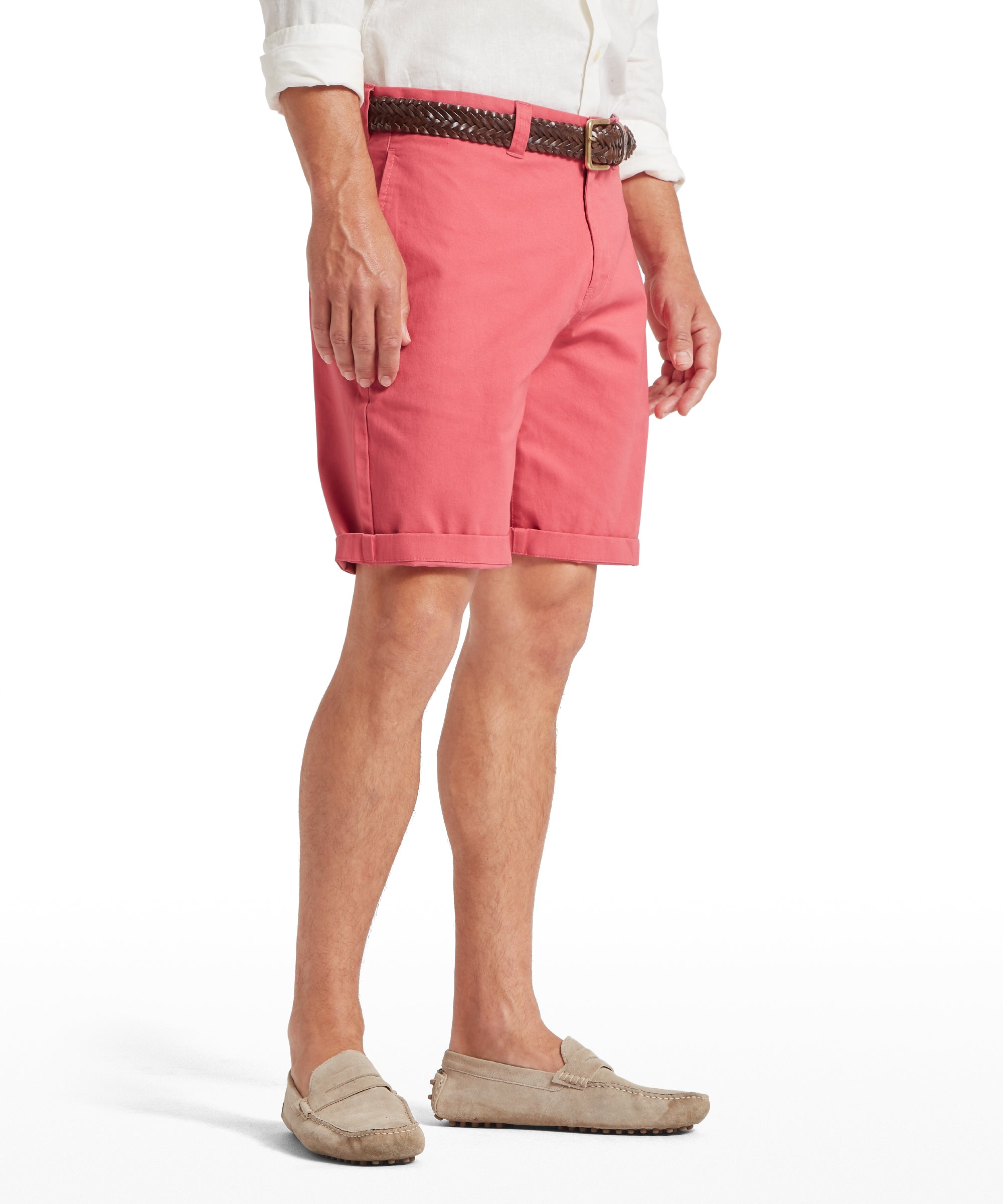 Man wearing pink rolled-up shorts paired with a white long-sleeved shirt with sleeves rolled up. Styled with a brown braided belt and beige loafers. Standing front-facing against a plain white background.