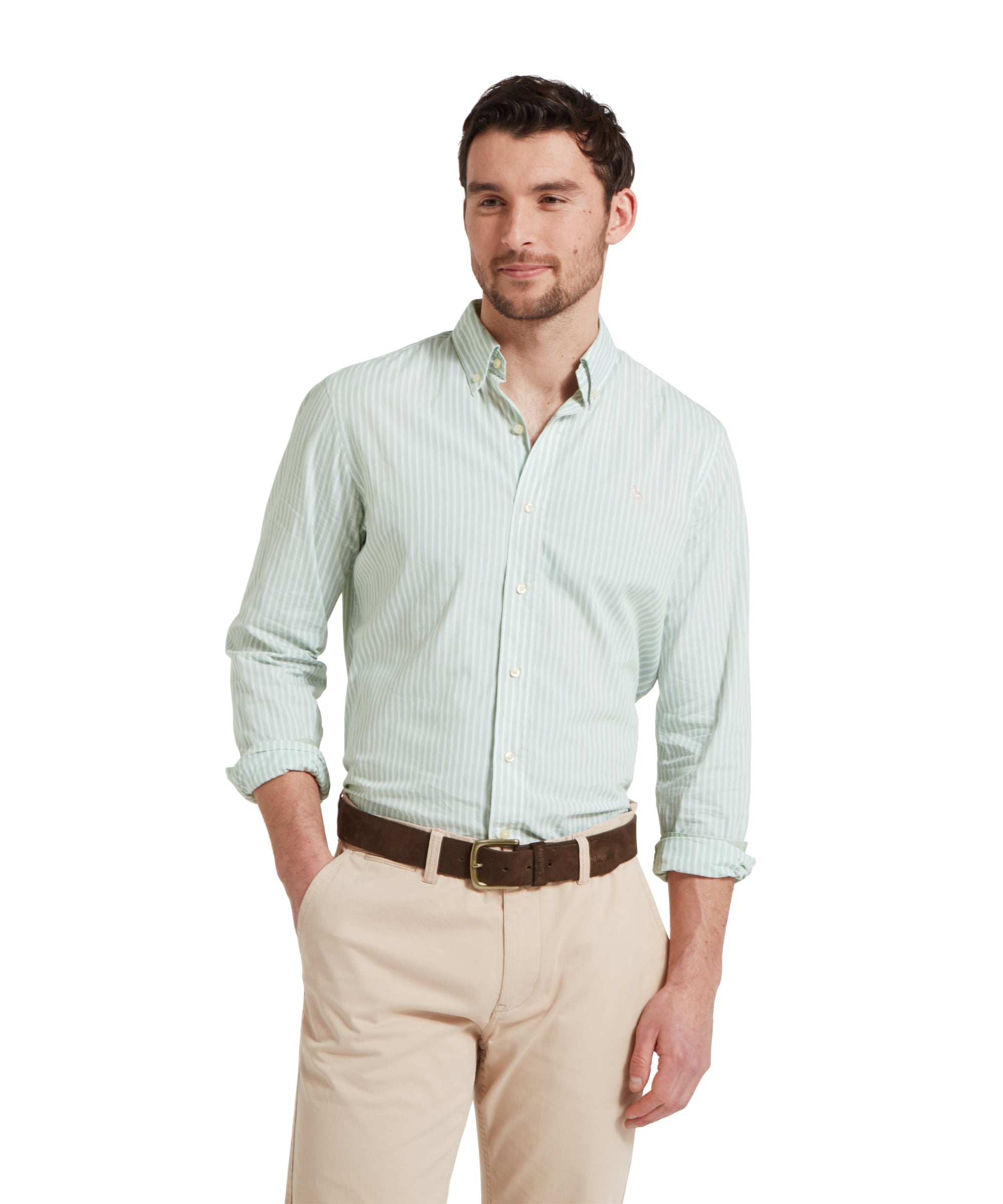 Close-up of a male model wearing a green and white striped Schöffel shirt, paired with beige chinos and a tan leather belt. He is standing in a relaxed pose with one hand in his pocket.