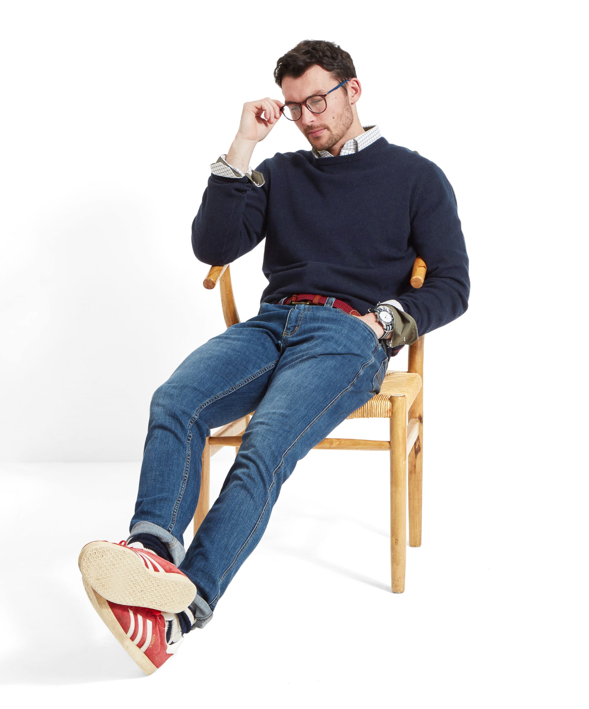 Man sitting on a chair wearing a navy knitted jumper, blue jeans, and red trainers.