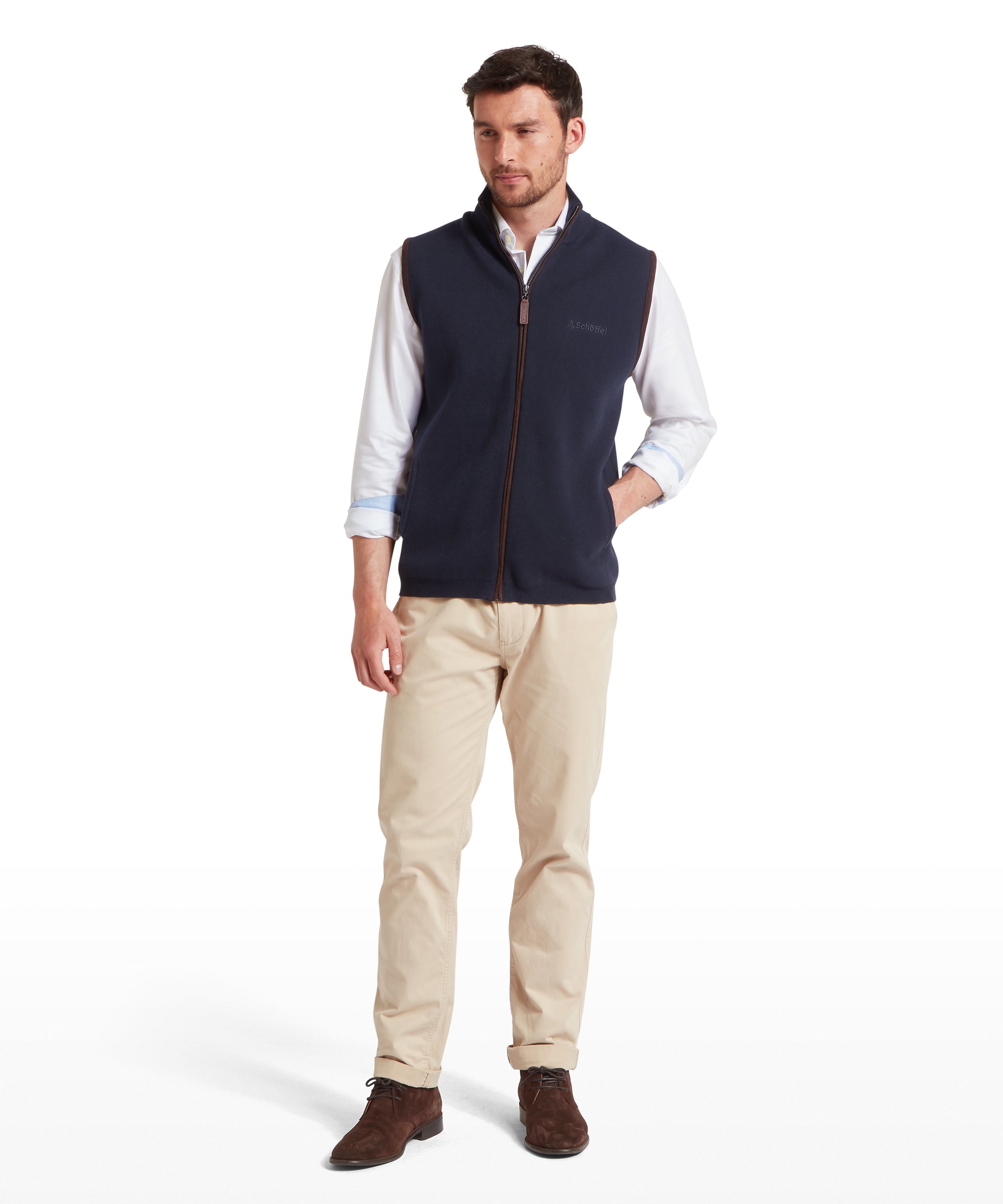 Man wearing a navy gilet over a white shirt with beige pants on a white background