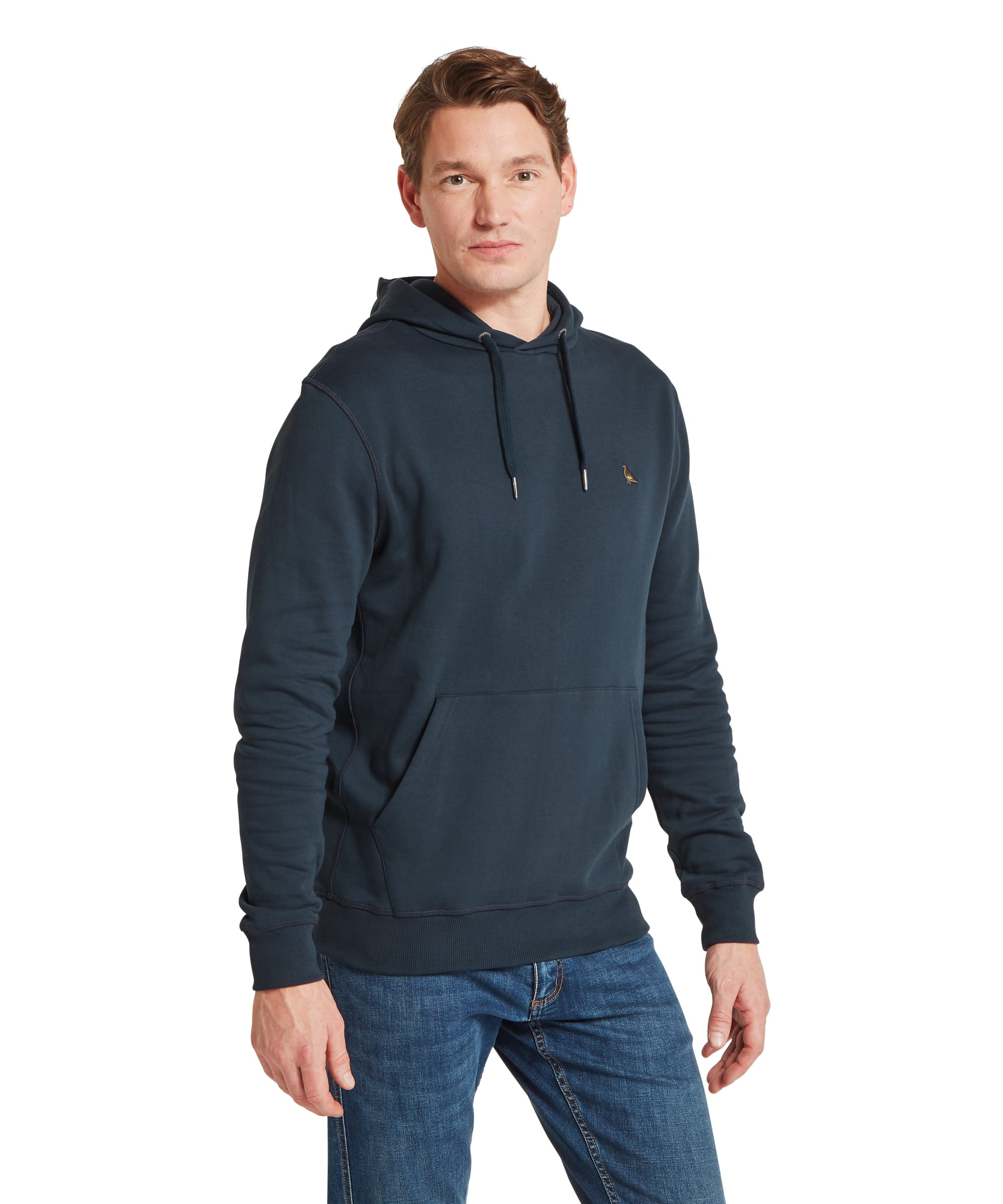 Schöffel Men's Pentire Heritage Hoodie in navy blue — front three-quarter view showing kangaroo pocket, embroidered pheasant logo and drawstring hood, styled with blue jeans and white trainers