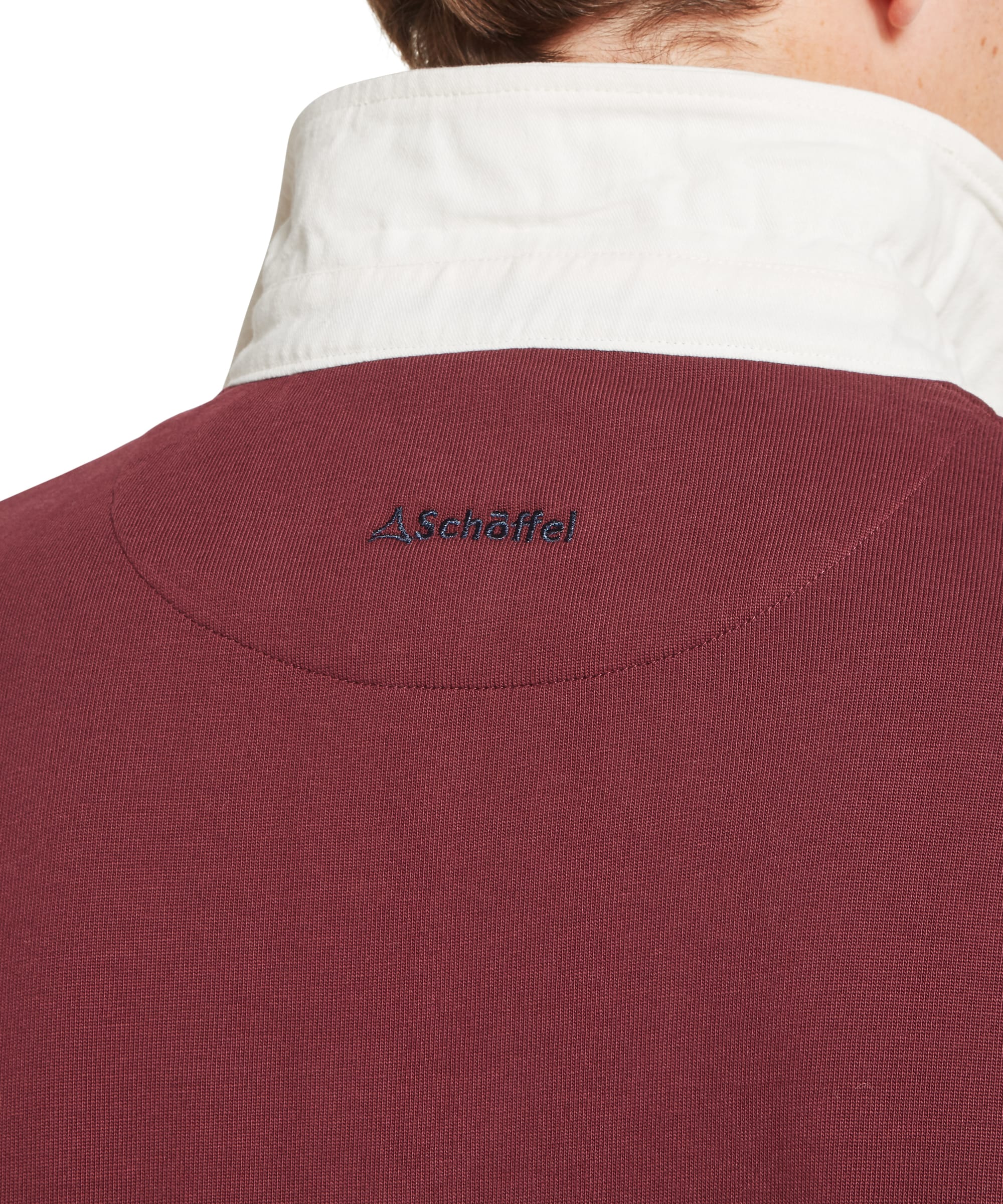 Schöffel Men's Porthallow Rugby Shirt in burgundy red — rear view showing Schöffel embroidered logo at the nape, clean back panel and ribbed cuffs, worn with dark blue jeans