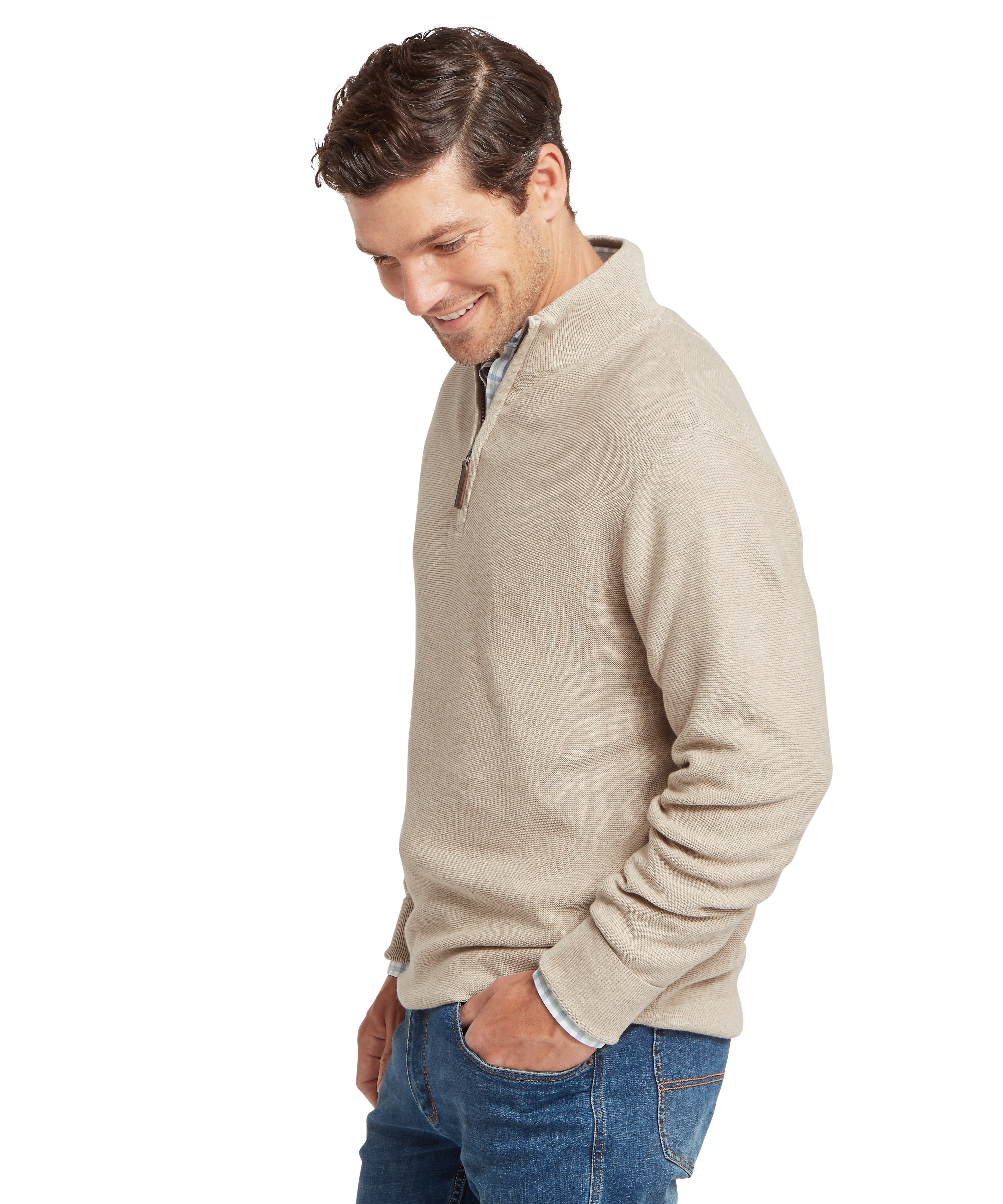 Man wearing a beige half-zip sweater and blue jeans  facing sideways against  a white background