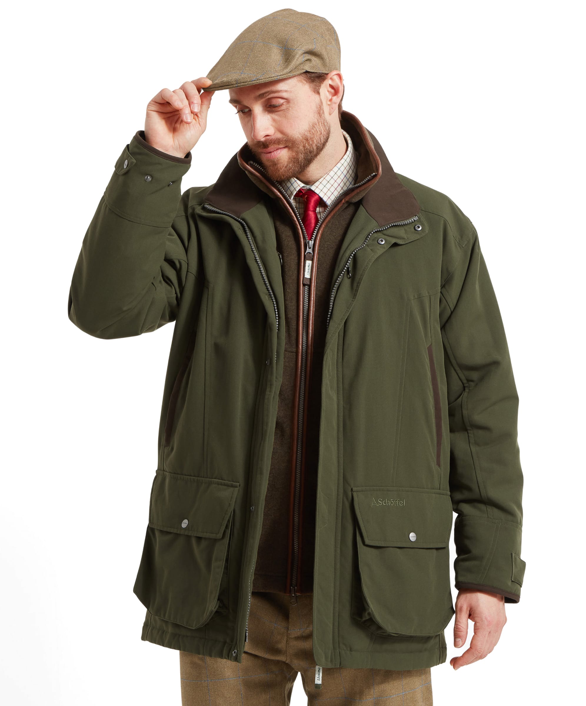 Schöffel Men's Ptarmigan Classic Coat in dark olive green — front view showing brown leather-trim collar, dual front zip, bellows pockets with press-stud flaps and shooting patch, styled with tweed plus-twos, Le Chameau wellington boots and a tweed flat cap
