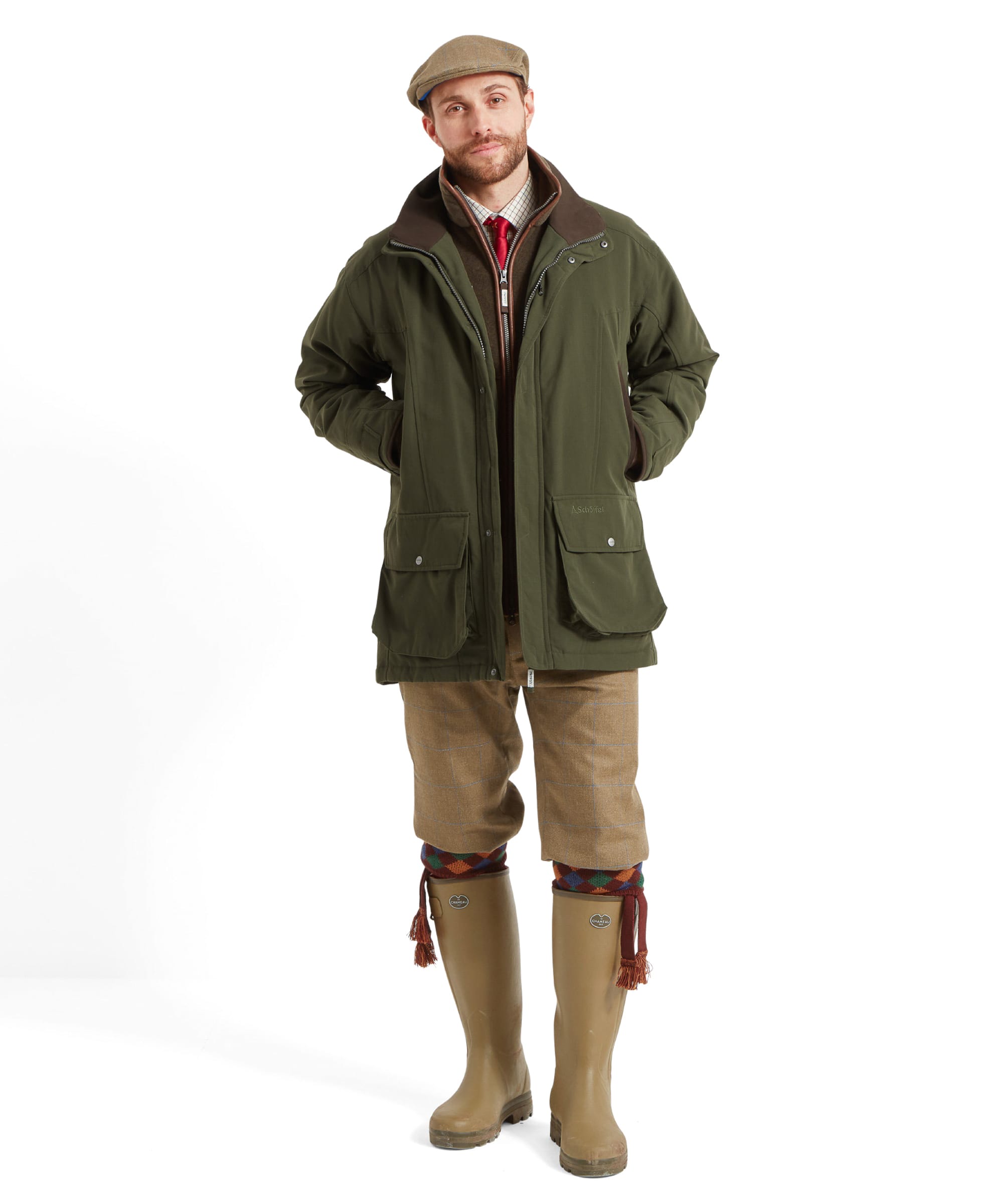 Schöffel Men's Ptarmigan Classic Coat in dark olive green — three-quarter front view showing structured silhouette, brown leather-trim collar, Schöffel logo and large bellows pockets, worn with tweed trousers and a tweed flat cap