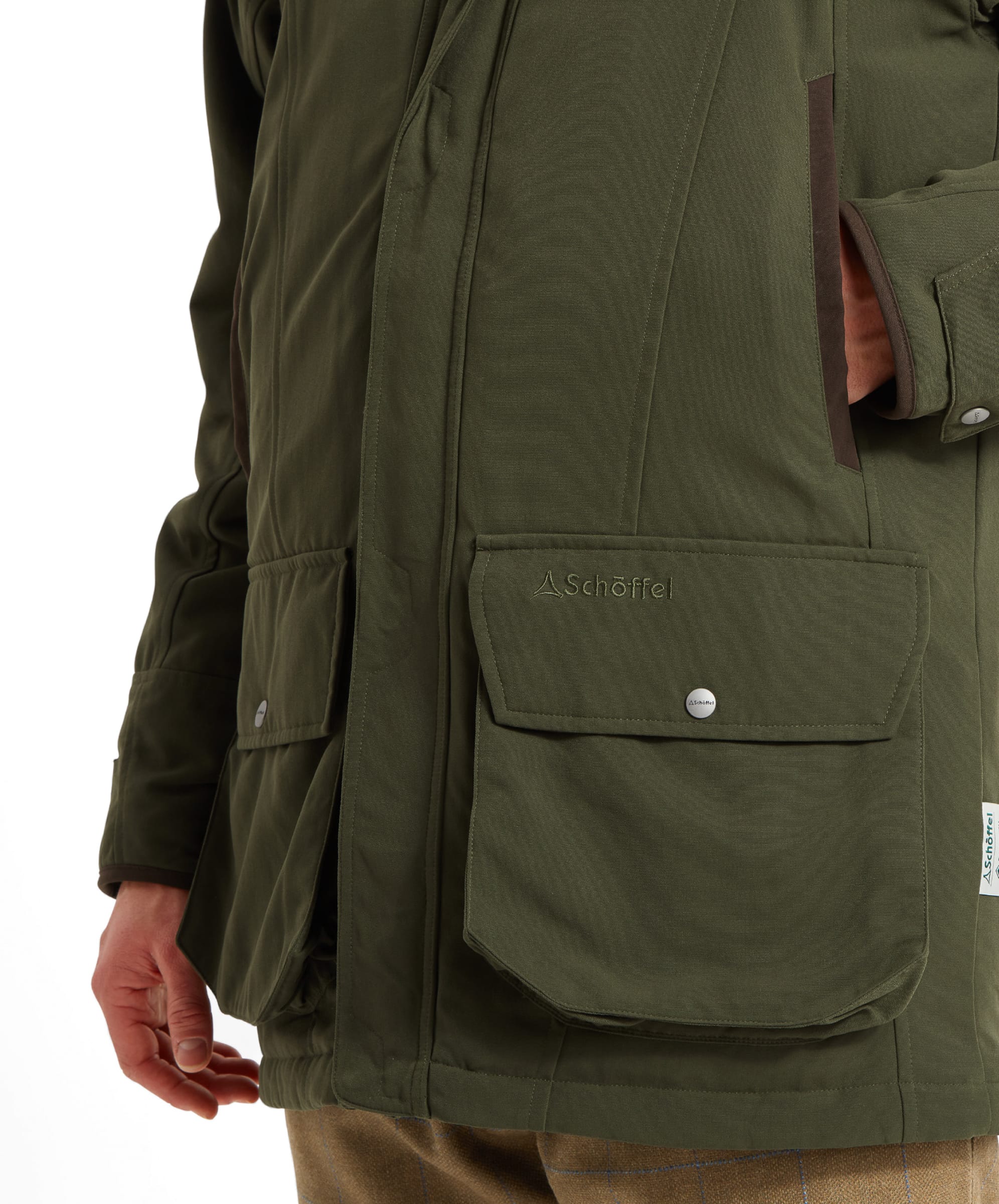 Schöffel Men's Ptarmigan Classic Coat in dark olive green — close-up of the deep bellows handwarmer pocket with brown leather trim binding, press-stud flap and Schöffel woven label at the hem