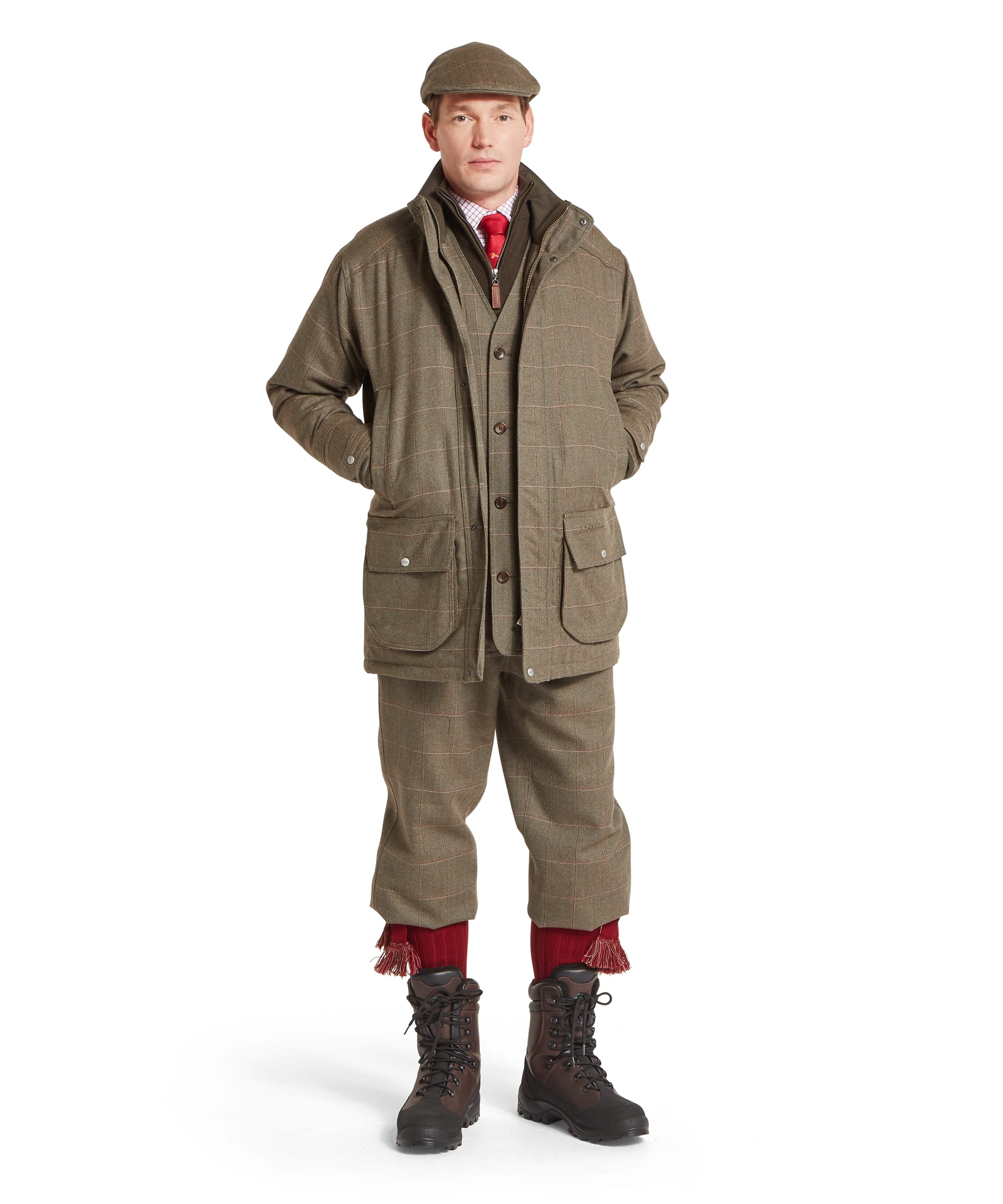 Schöffel Men's Ptarmigan Tweed Classic Coat in Lovat brown windowpane check — full-length front view showing matching tweed shooting suit with coat and plus twos, layered over a zip-neck gilet, checked shirt and red tie, worn with country boots and red sock garters, styled with a tweed flat cap