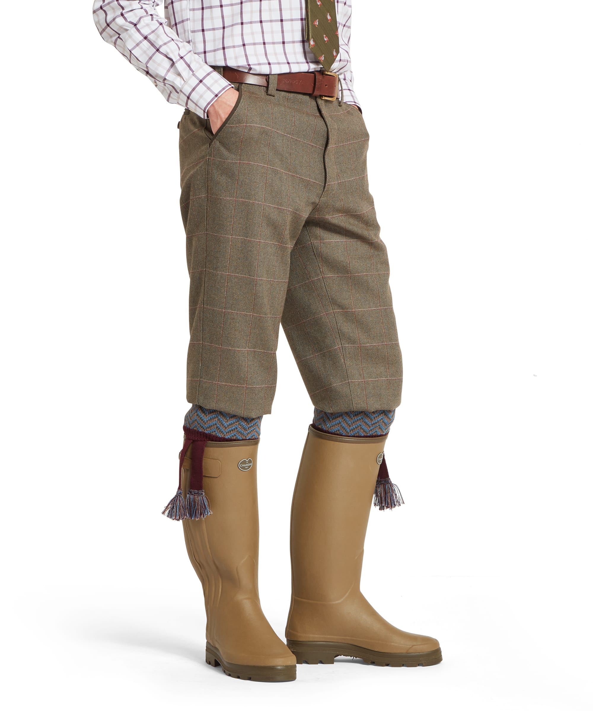 Schöffel Men's Ptarmigan Tweed Plus Twos in Lovat brown Lochlane windowpane check — side view showing the generous plus-two cut, side pocket opening and gathered hem below the knee, worn with Le Chameau wellington boots and patterned chevron sock garters