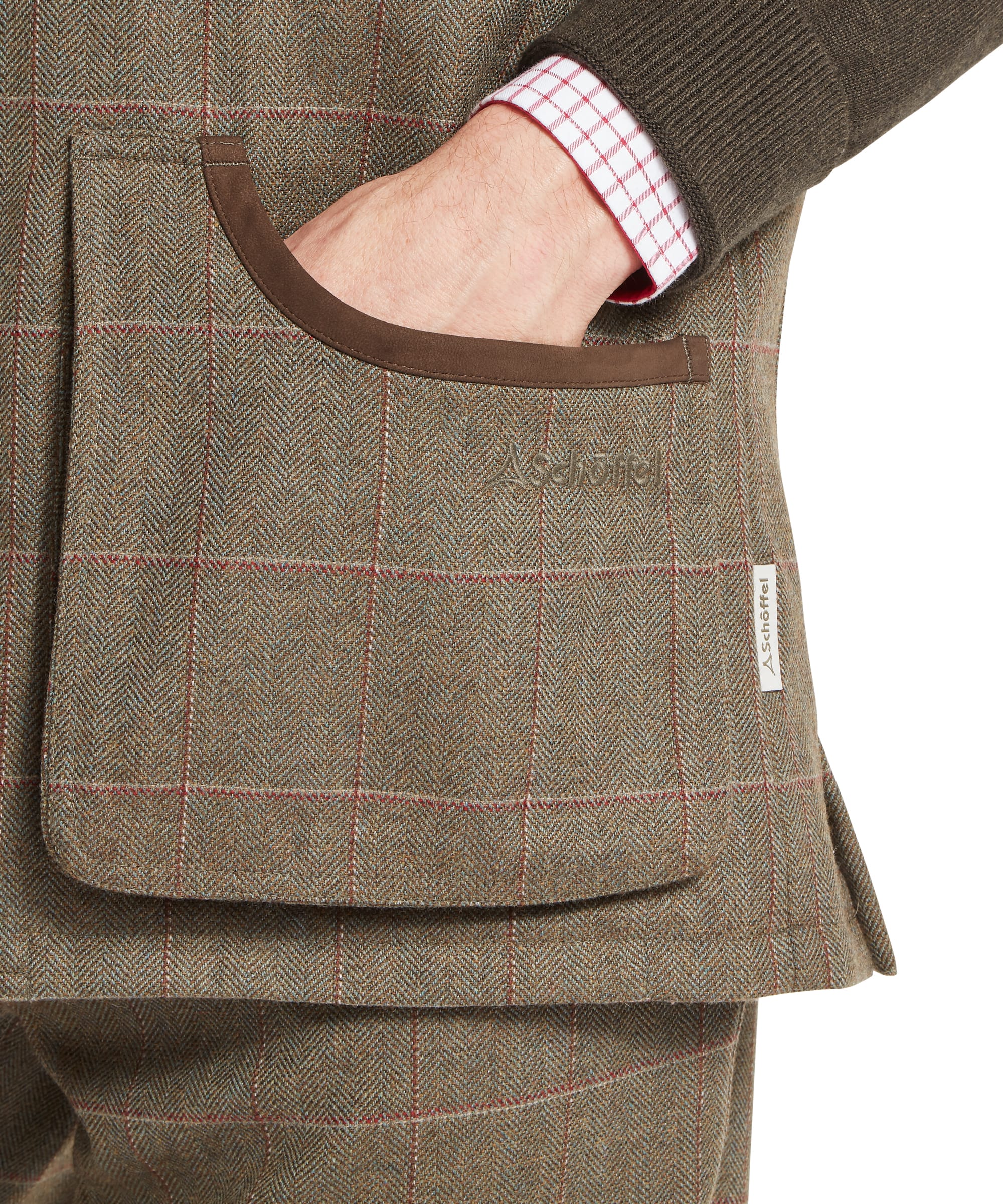 Schöffel Men's Ptarmigan Tweed Waistcoat II in Lovat brown windowpane check — close-up of the lower body showing deep lower patch pocket with brown suede leather binding, hand inside the opening, Schöffel embroidered logo and woven label on the Lochlane tweed fabric