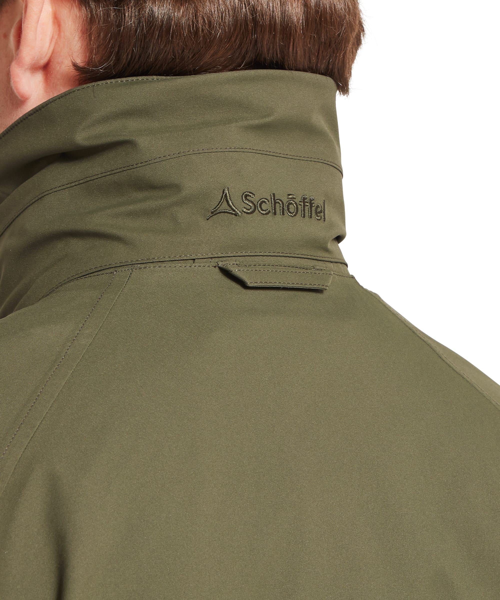 Schöffel Men's Snipe Ultralight Coat in dark olive green — rear three-quarter view showing the elasticated back waist drawcord, vertical side zip pocket, Schöffel woven label at the hem and articulated elbow seaming, worn with tweed plus twos and a tweed flat cap