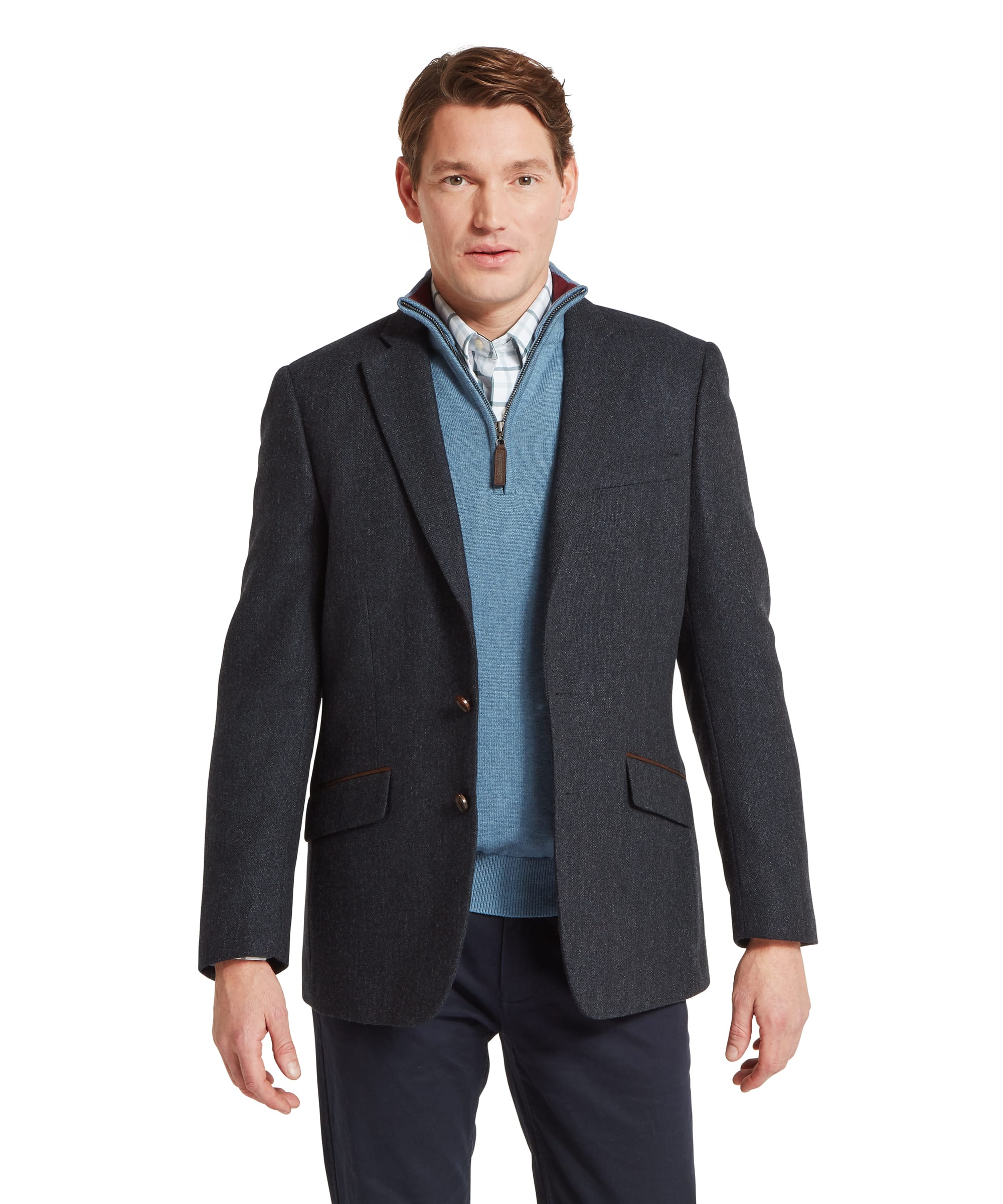 Schöffel Men's St Andrews Tweed Sports Jacket in navy herringbone — front view showing two-button tailored sports jacket silhouette in dark navy Lovat Tweed woven in Scotland, with notched lapels, flap lower pockets and suede-bound chest pocket, layered over a light blue zip-neck merino gilet and checked shirt, worn with navy trousers and brown suede tassel loafers