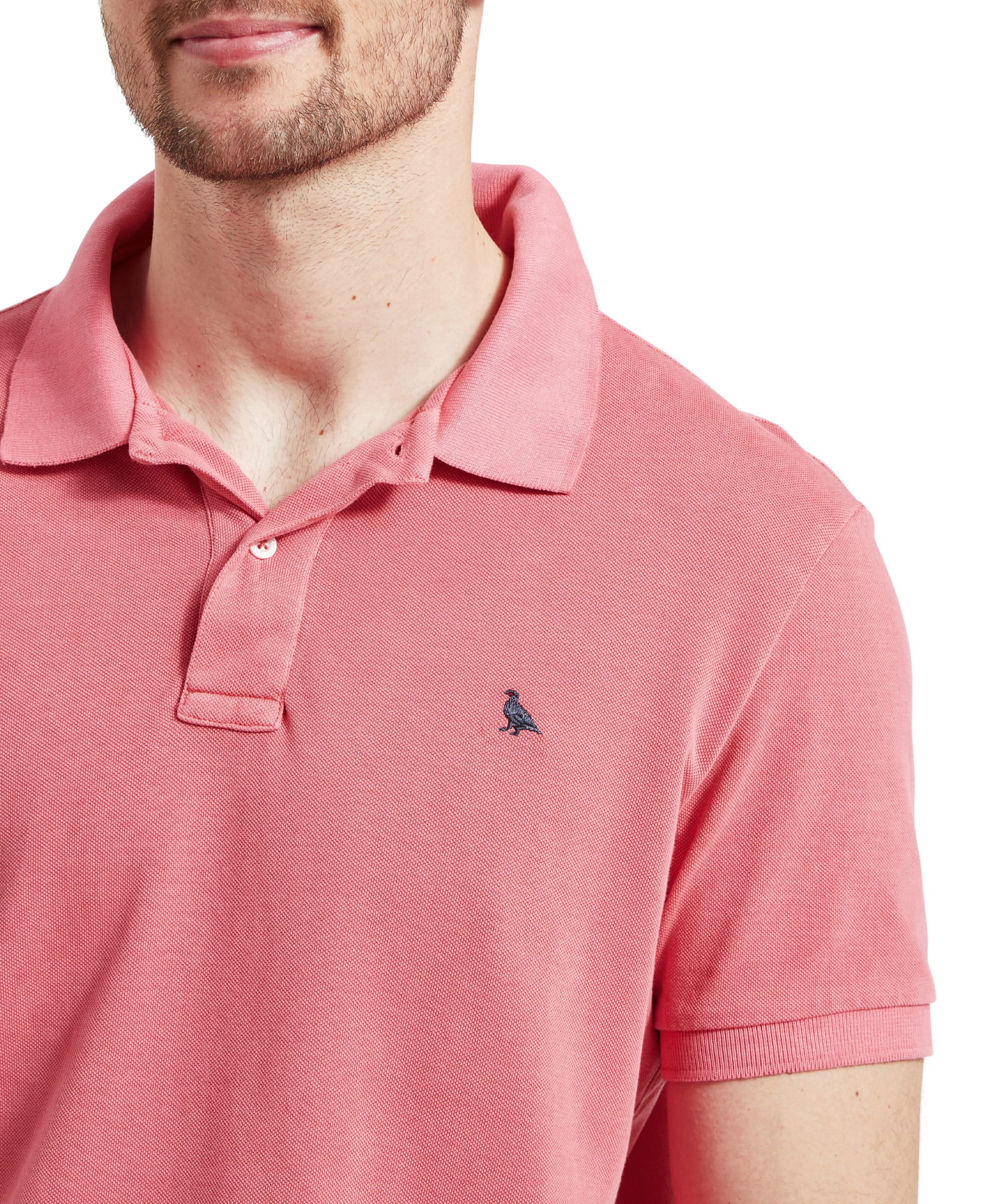 Schöffel Men's St Ives Garment Dyed Polo Shirt in coral pink, close-up on model showing embroidered navy grouse logo and two-button placket