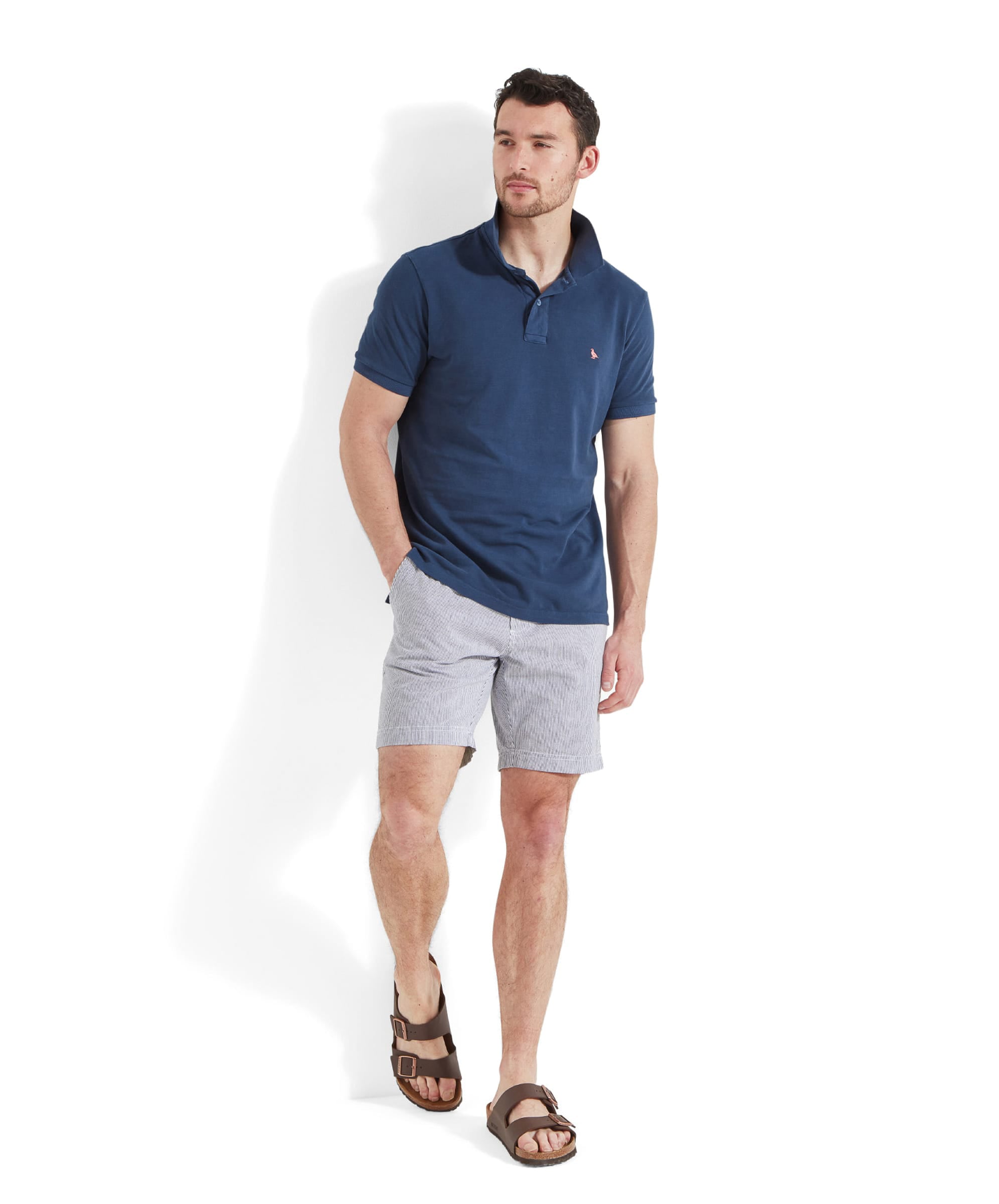 Schöffel Men's St Ives Garment Dyed Polo Shirt in denim blue, full-length view on model paired with striped shorts and sandals