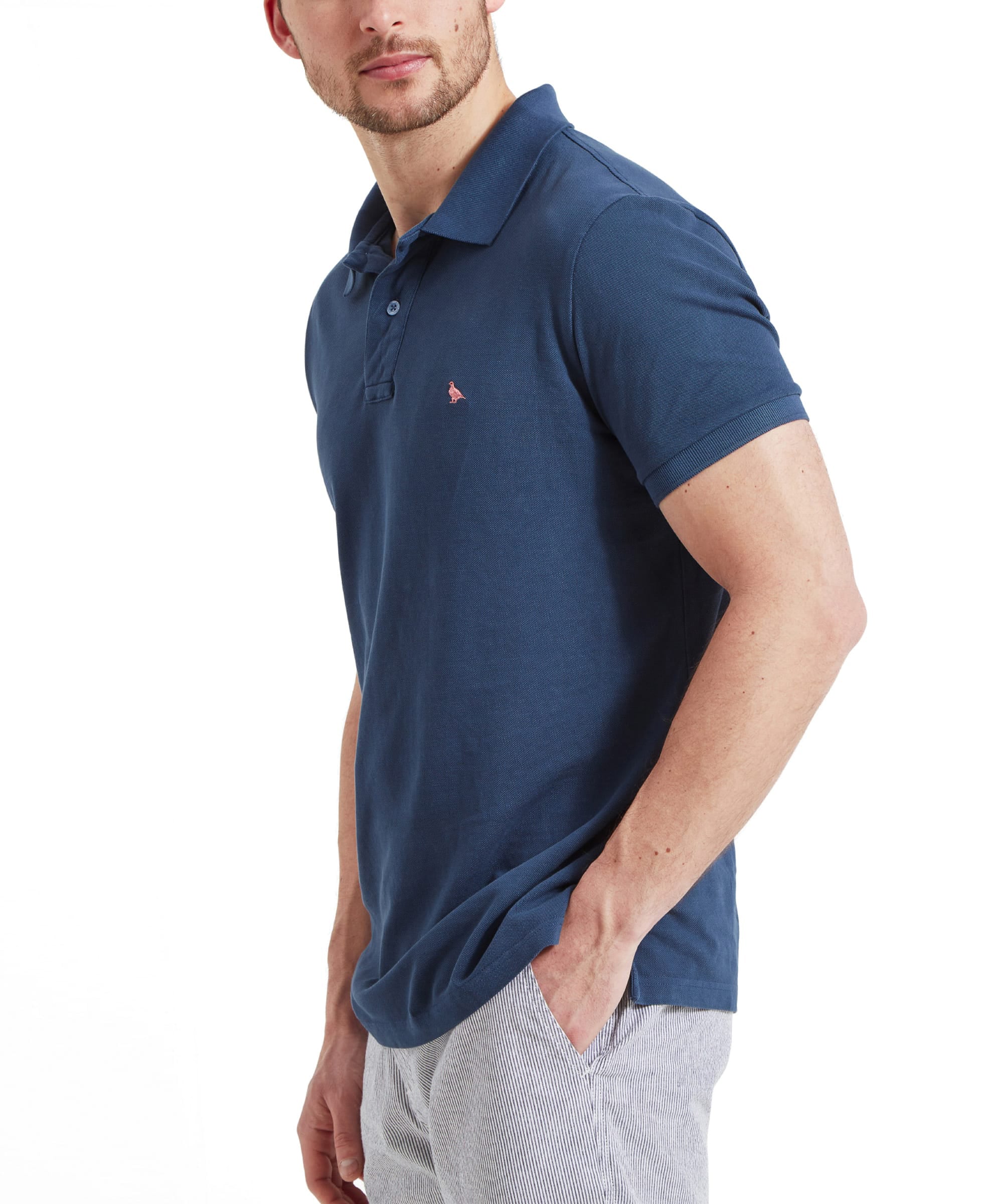 Schöffel Men's St Ives Garment Dyed Polo Shirt in denim blue, side profile on model styled with striped shorts, embroidered coral grouse motif