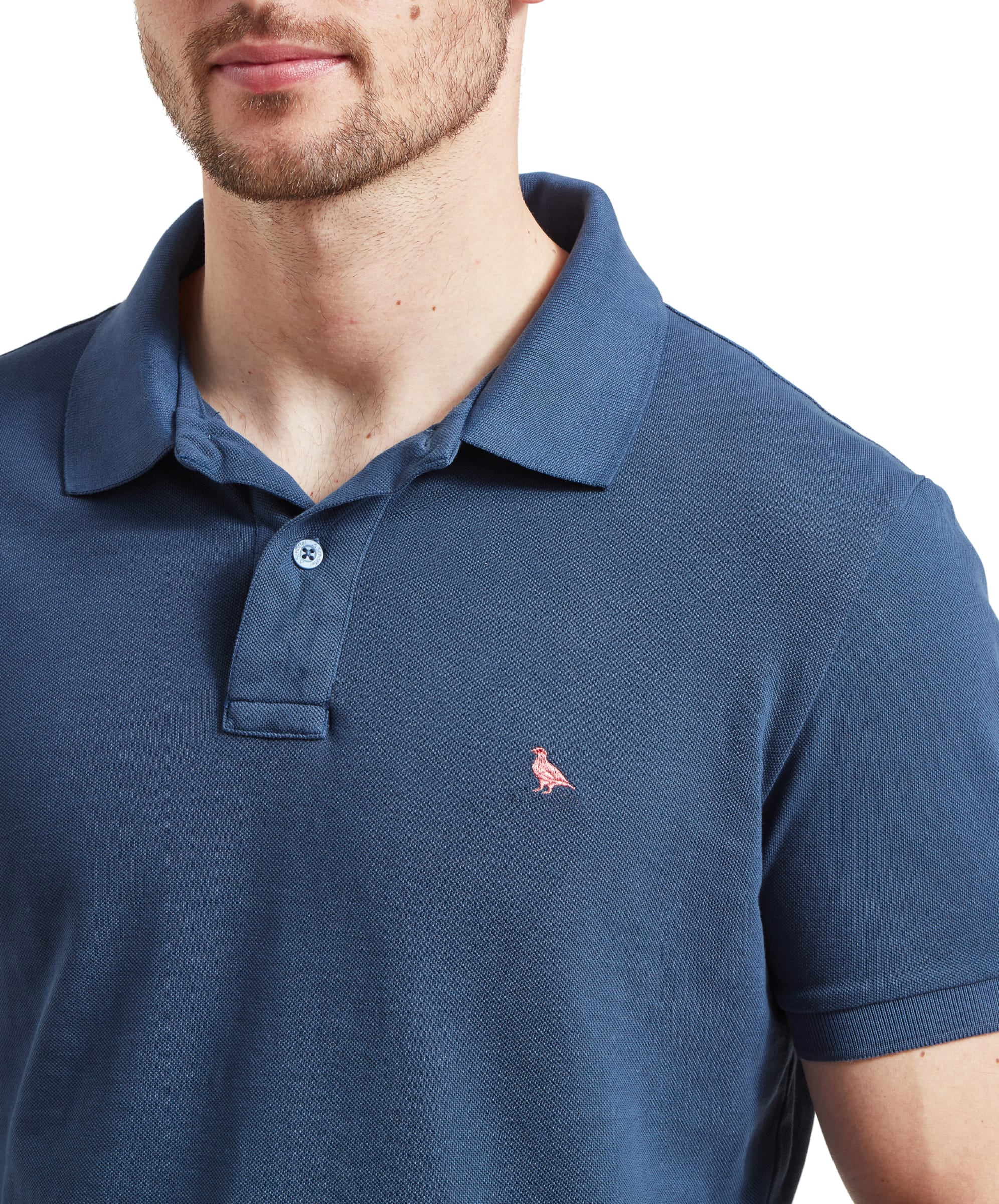Schöffel Men's St Ives Garment Dyed Polo Shirt in denim blue, close-up on model showing embroidered coral grouse logo and two-button placket