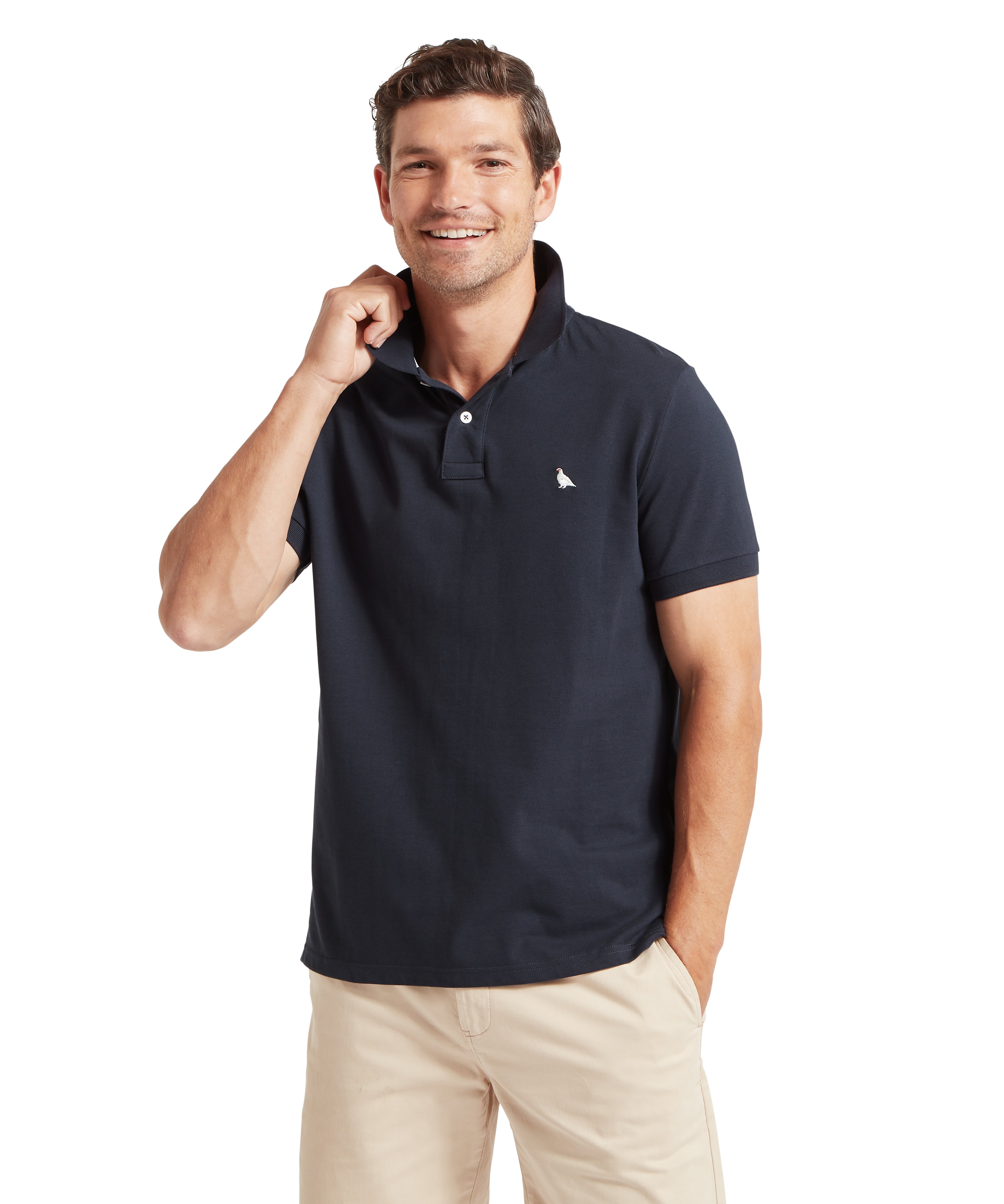 Man wearing a navy polo shirt with a small ptarmigan logo against a white background.  The man is facing towards the camera and has one hand in his pocket and the other adjusting his collar.