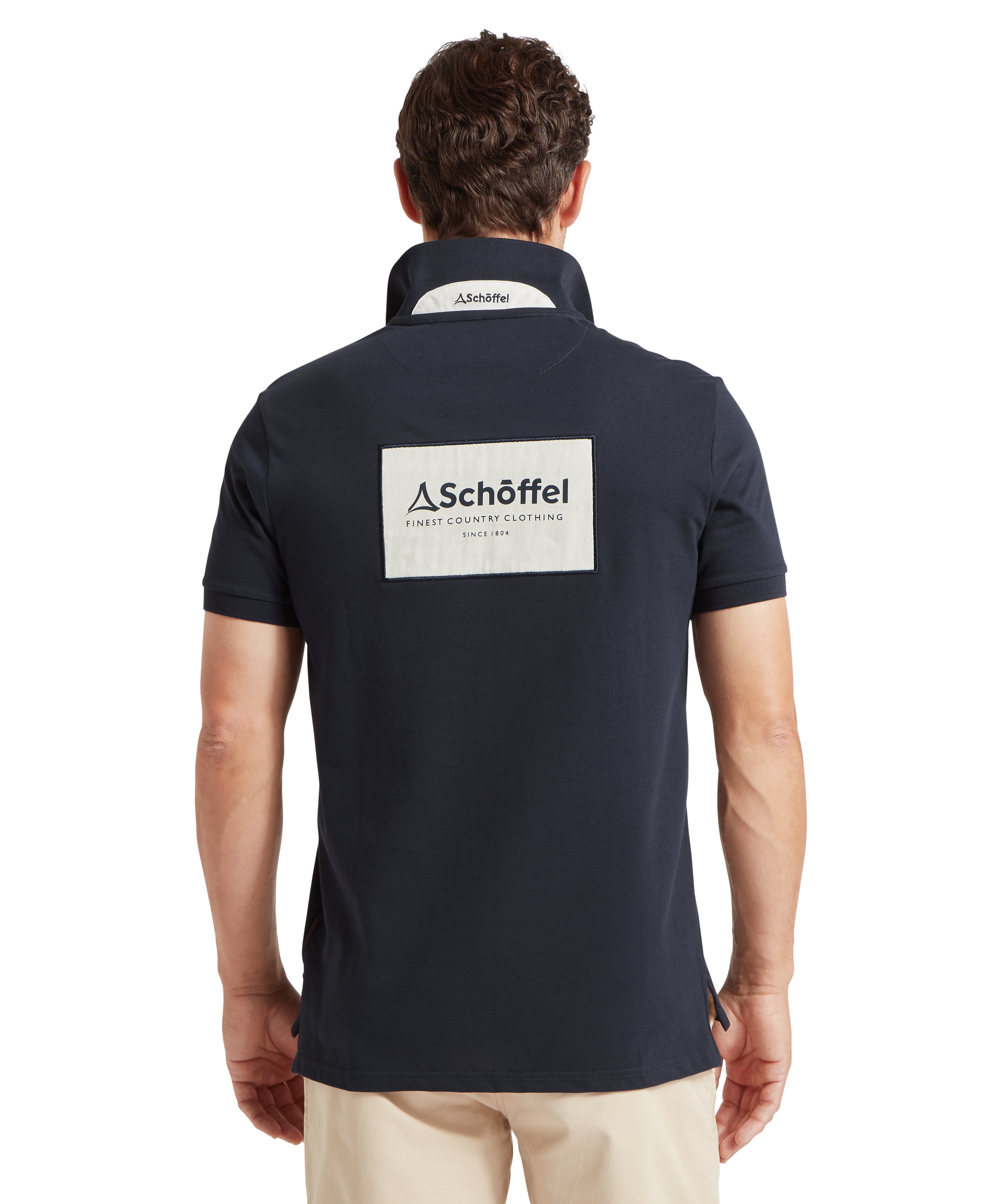Man wearing a navy polo shirt with a Schöffel logo on the back and neck standing backwards against a white background