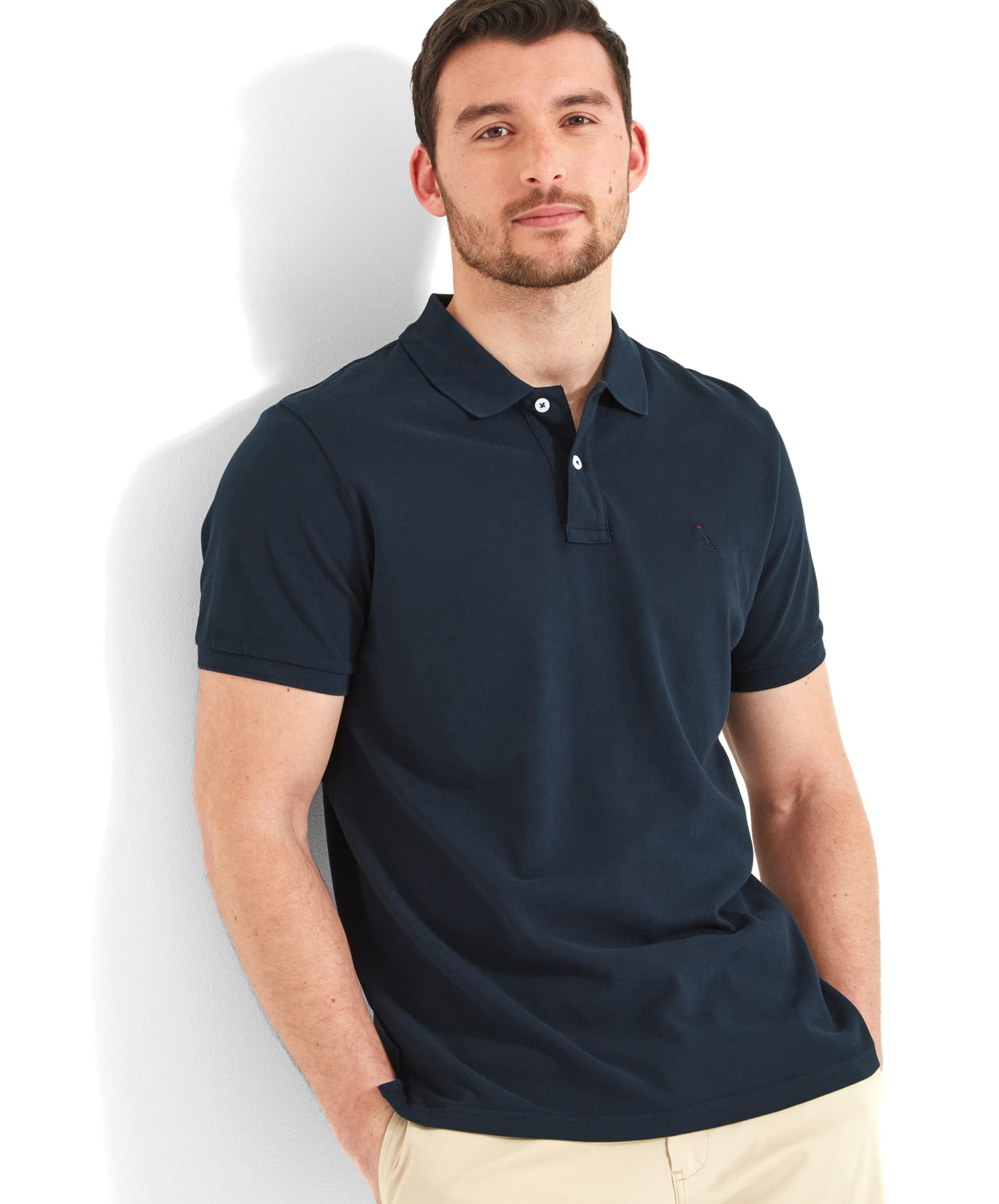 Schöffel Men's St Ives Polo Shirt in navy, worn by model leaning against wall with beige shorts