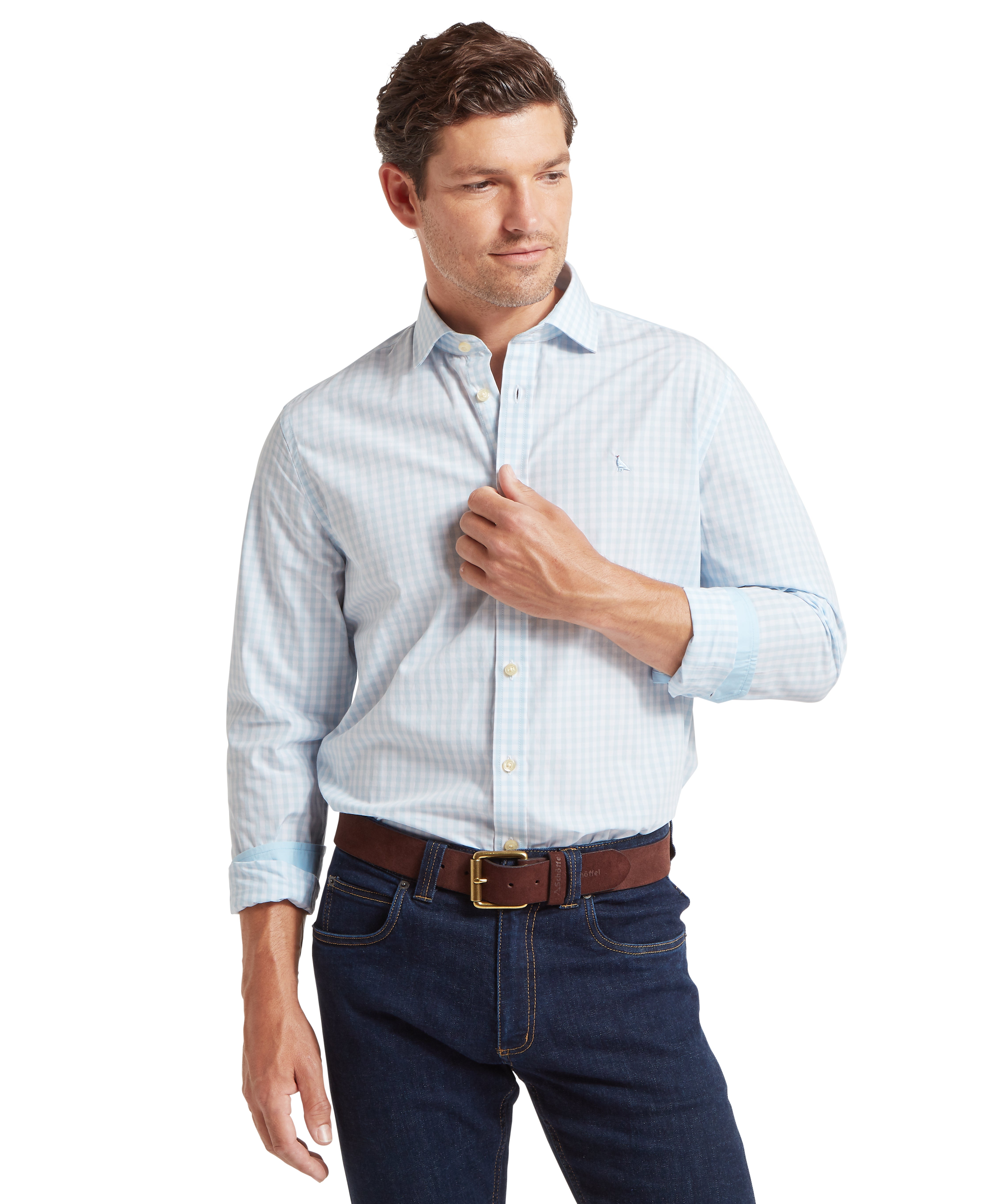 Man wearing a light blue checked shirt, dark jeans and brown belt against a white background.