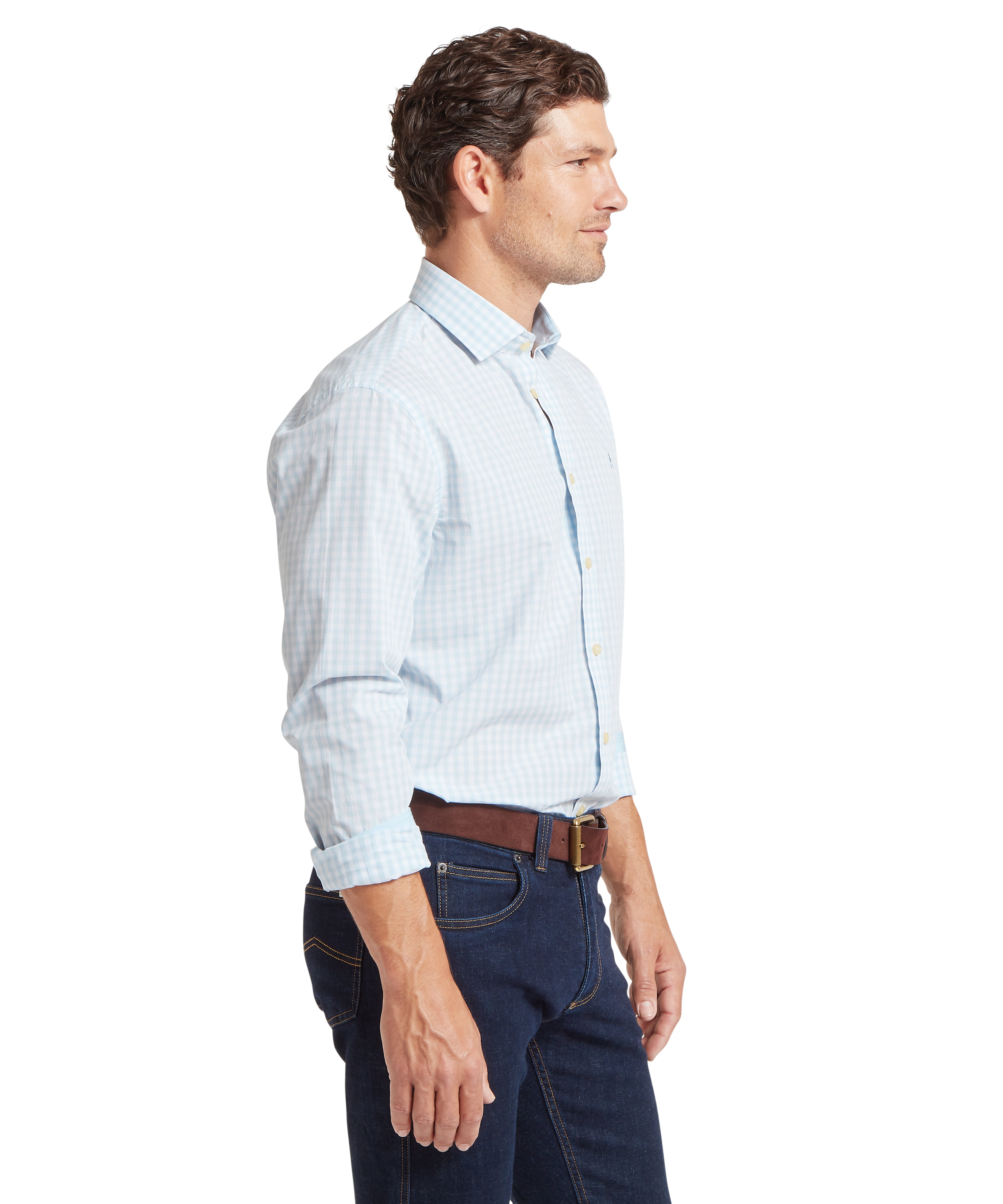 Man wearing a light blue checked shirt and dark jeans facing sideways against a white background